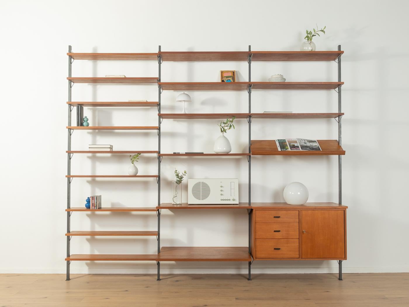 Wonderful shelving system in teak veneer from the 1960s. The system consists of four black metal ladders, 18 shelves, one magazine rack and one container with three drawers, one door and one shelf.

Quality Features:
high quality materials
very good