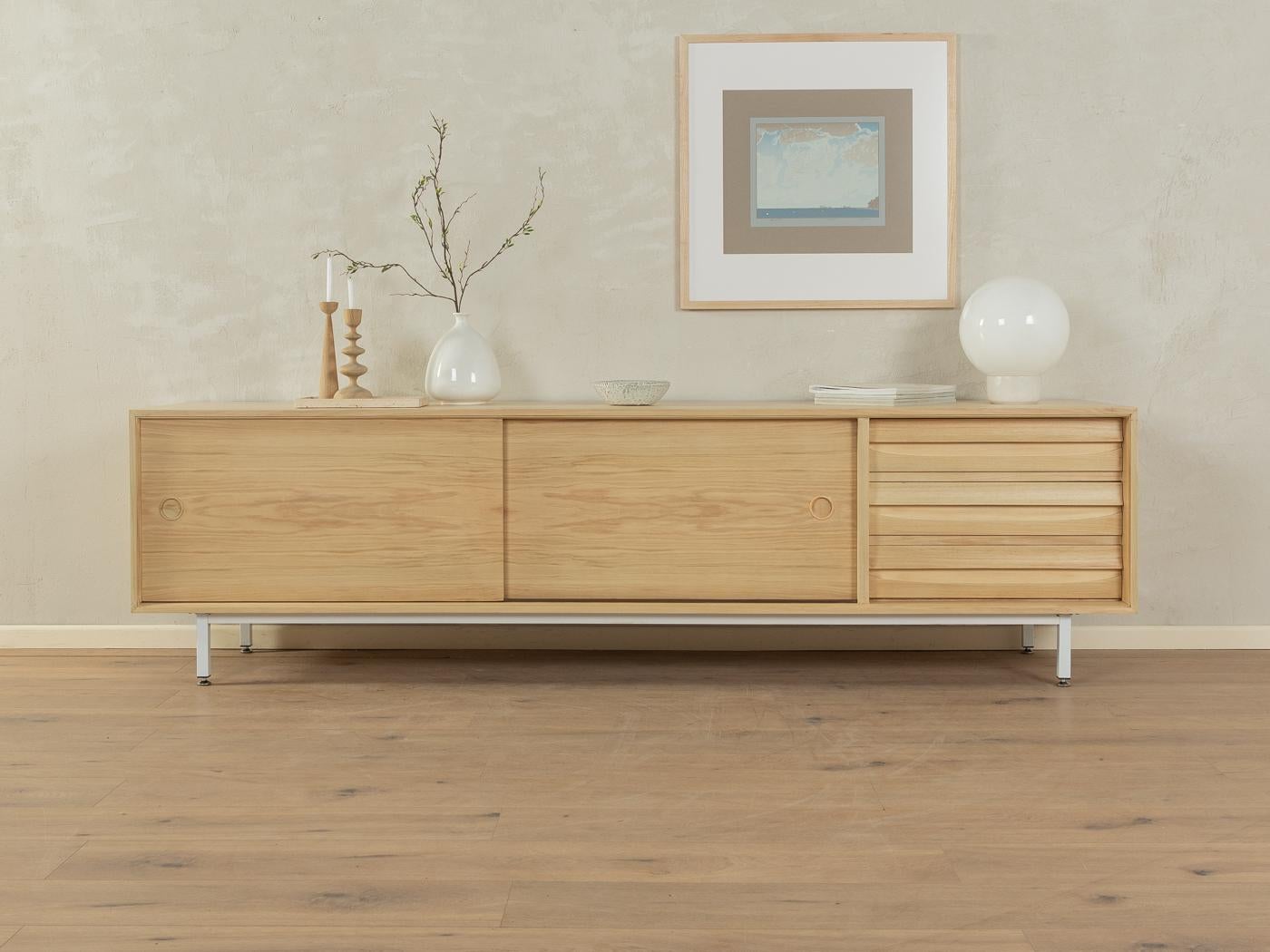 Einzigartiges Sideboard aus den 1960er Jahren von Lothar Wegner. Corpus in gebleichtem Nussbaumfurnier mit drei Schubladen, zwei Schiebetüren, zwei Einlegeböden und neuen Vierkantstahlfüßen in Weiß.
Qualitätsmerkmale:

    sehr gute Verarbeitung
   