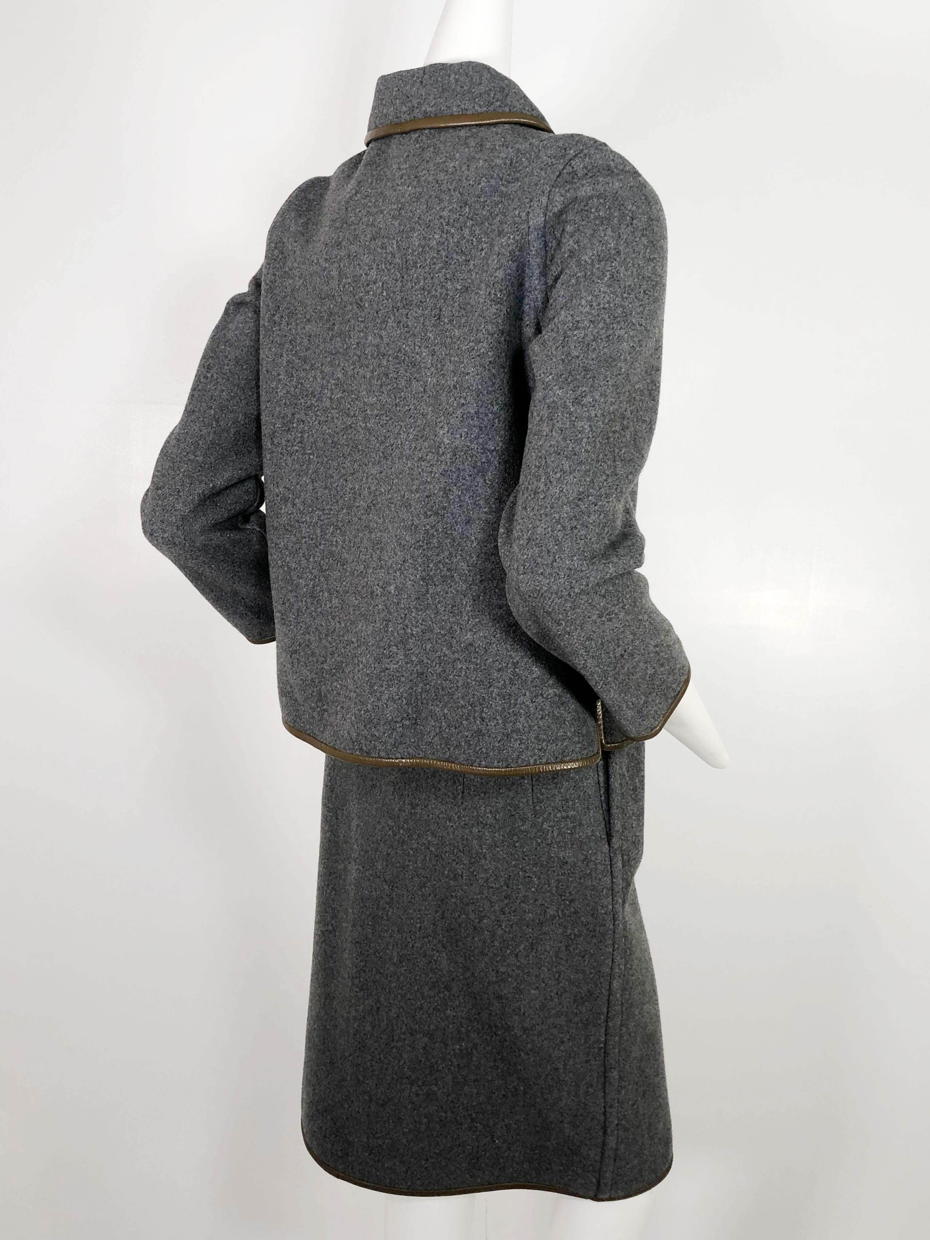 A beautiful, simply styled, 1960s Mod, Sills by Bonnie Cashin, gray wool skirt suit with Cashin's signature leather trim in tobacco brown. Skirt is cut straight with wrap around front button closures. Jacket has a slight A-line cut. Impeccably