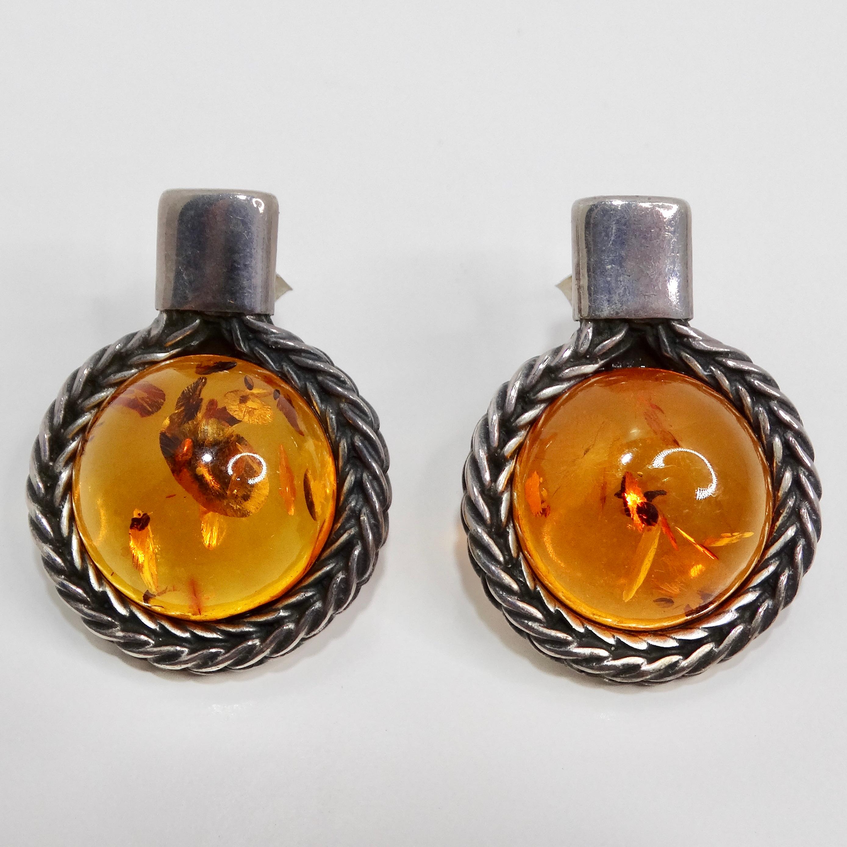 Les boucles d'oreilles d'ambre en argent des années 1960 sont une magnifique paire vintage qui capture l'élégance intemporelle et l'allure vibrante de l'ambre. Ces superbes boucles d'oreilles sont ornées de pierres d'ambre rondes, chacune présentant