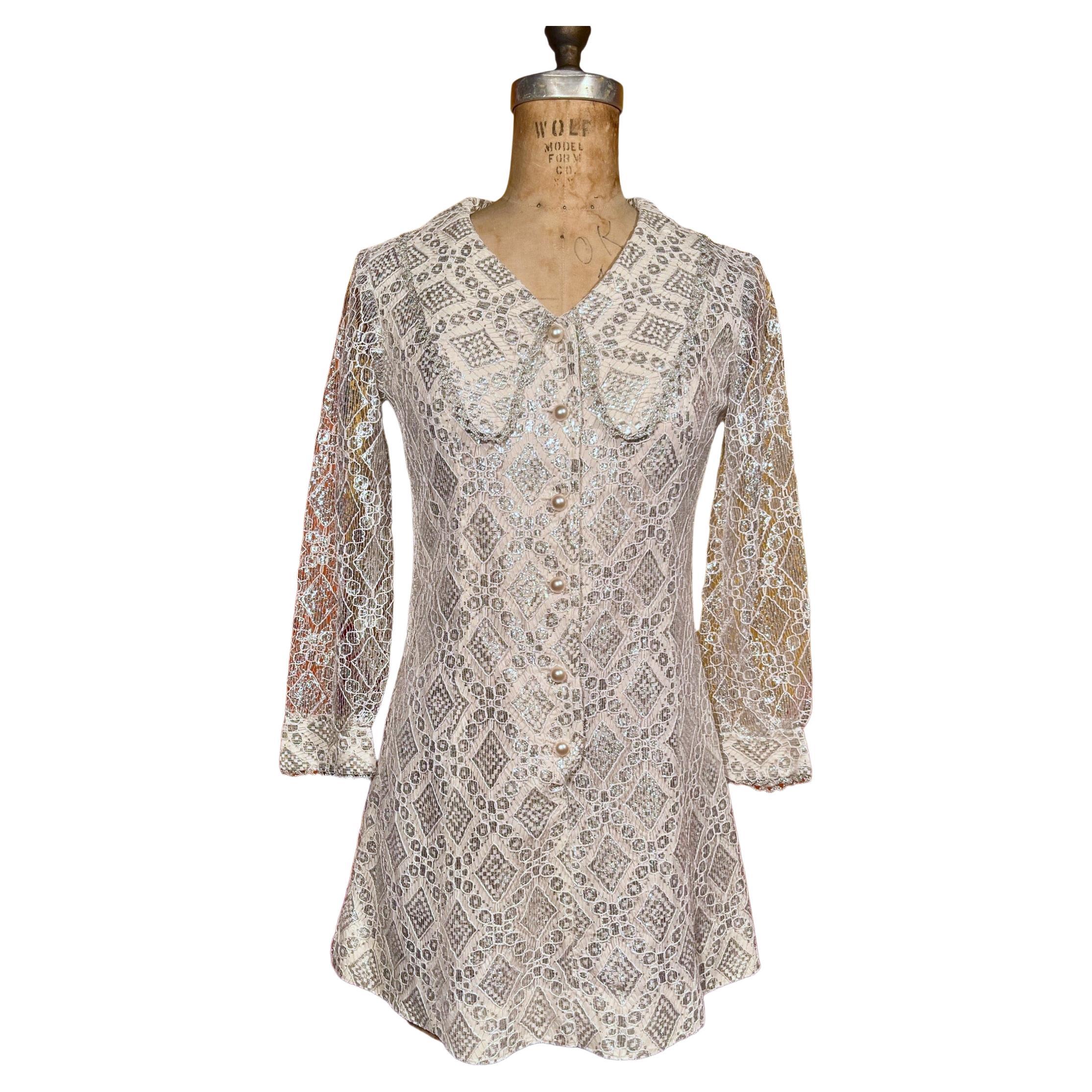 Incredible 1960’s silver metallic lace mini dress with white sleeveless lining, metallic threading, sheer sleeves, pearly buttons and dramatic wide lapels. No labels aside from 