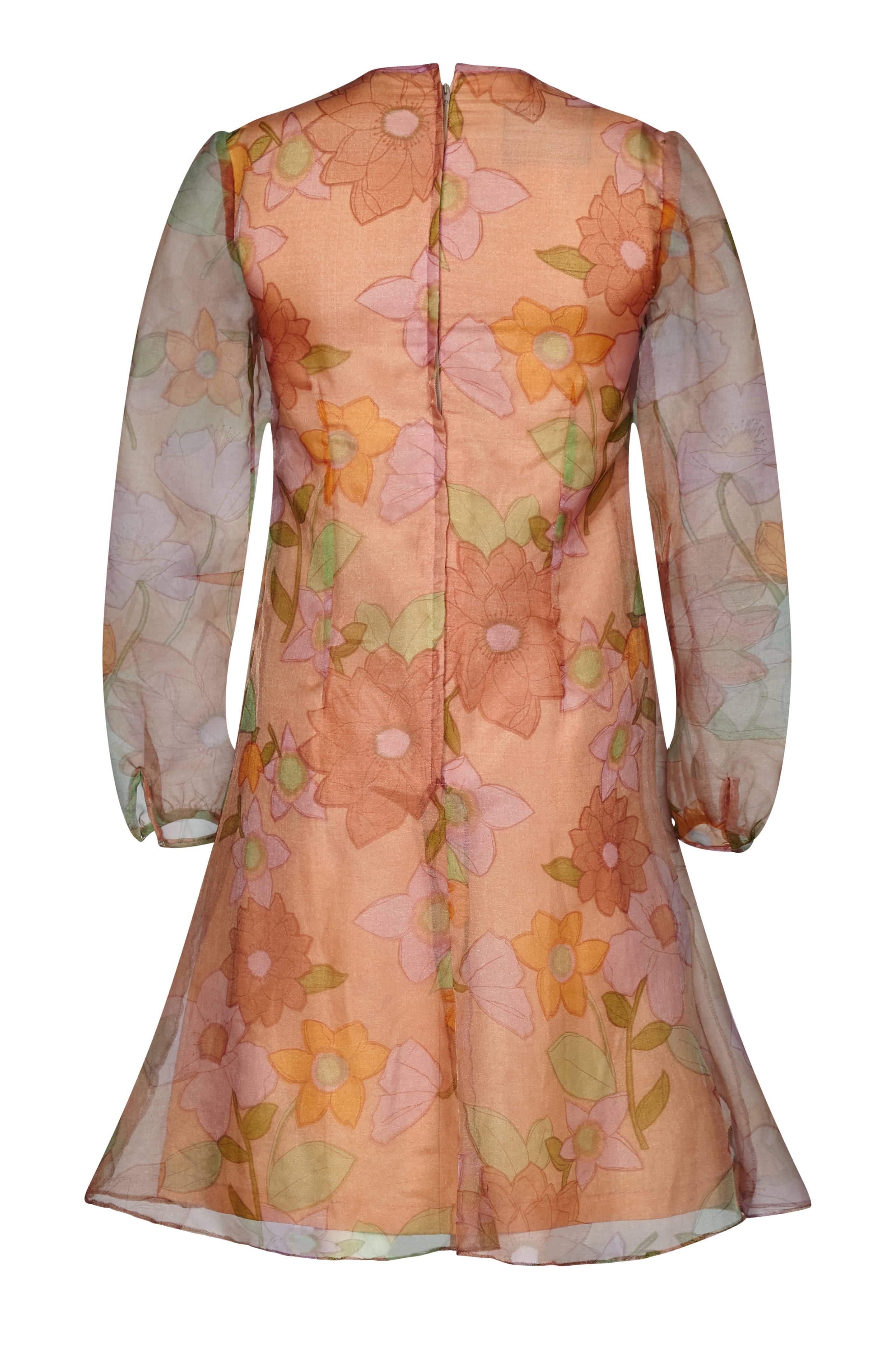 Cette robe à imprimé floral en nylon organza de Simon Massey des années 1960 incarne parfaitement le style et l'ambiance des boutiques londoniennes. La créatrice a choisi un imprimé floral graphique audacieux adouci par des tons chauds et subtils de