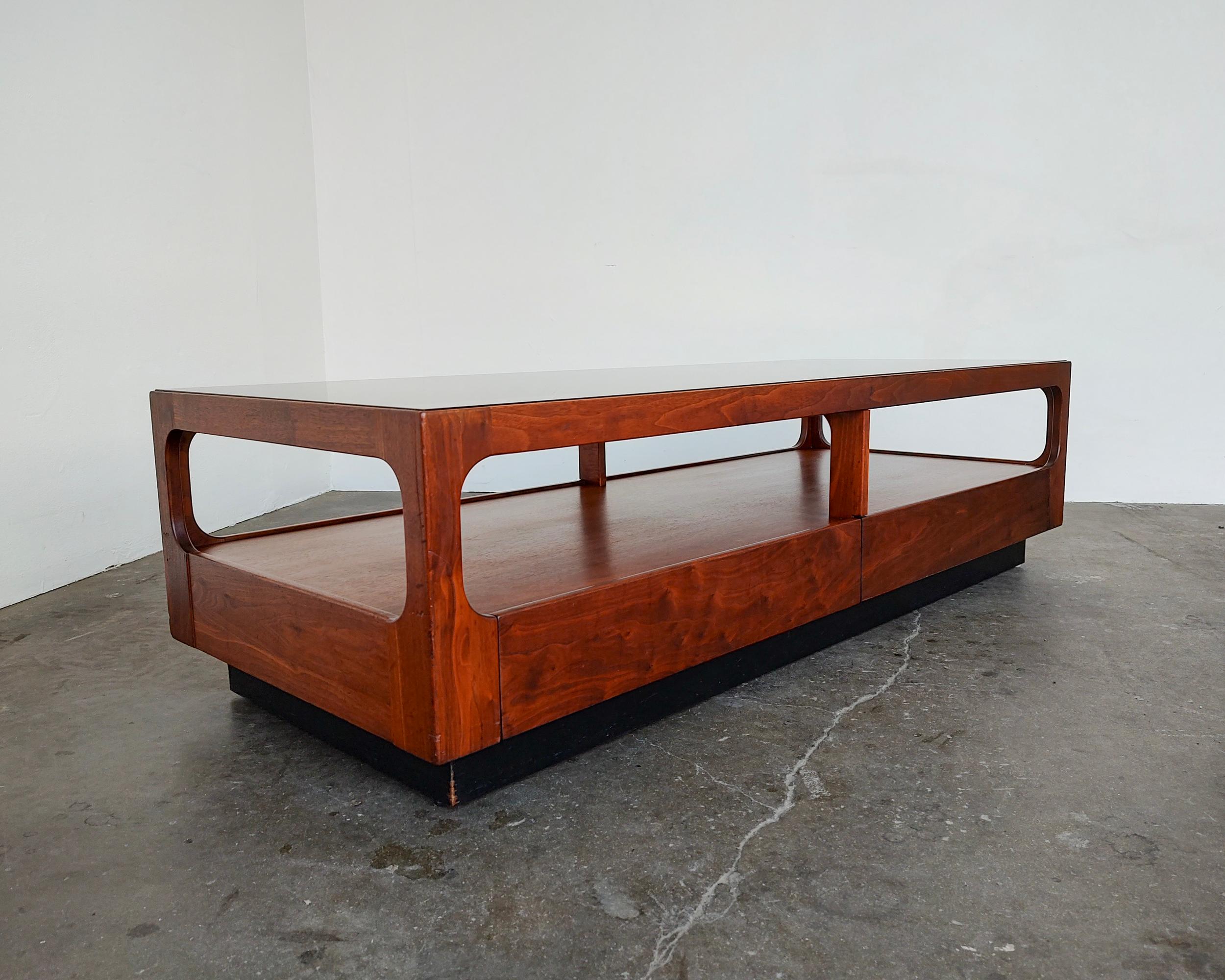Classic mid-century modern walnut wood and smokey glass coffee table designed by John Keal for Brown Saltman. Contrasting platform black base. Features one drawer with original label inside. Glass in excellent condition, no scratches or chips. Wood