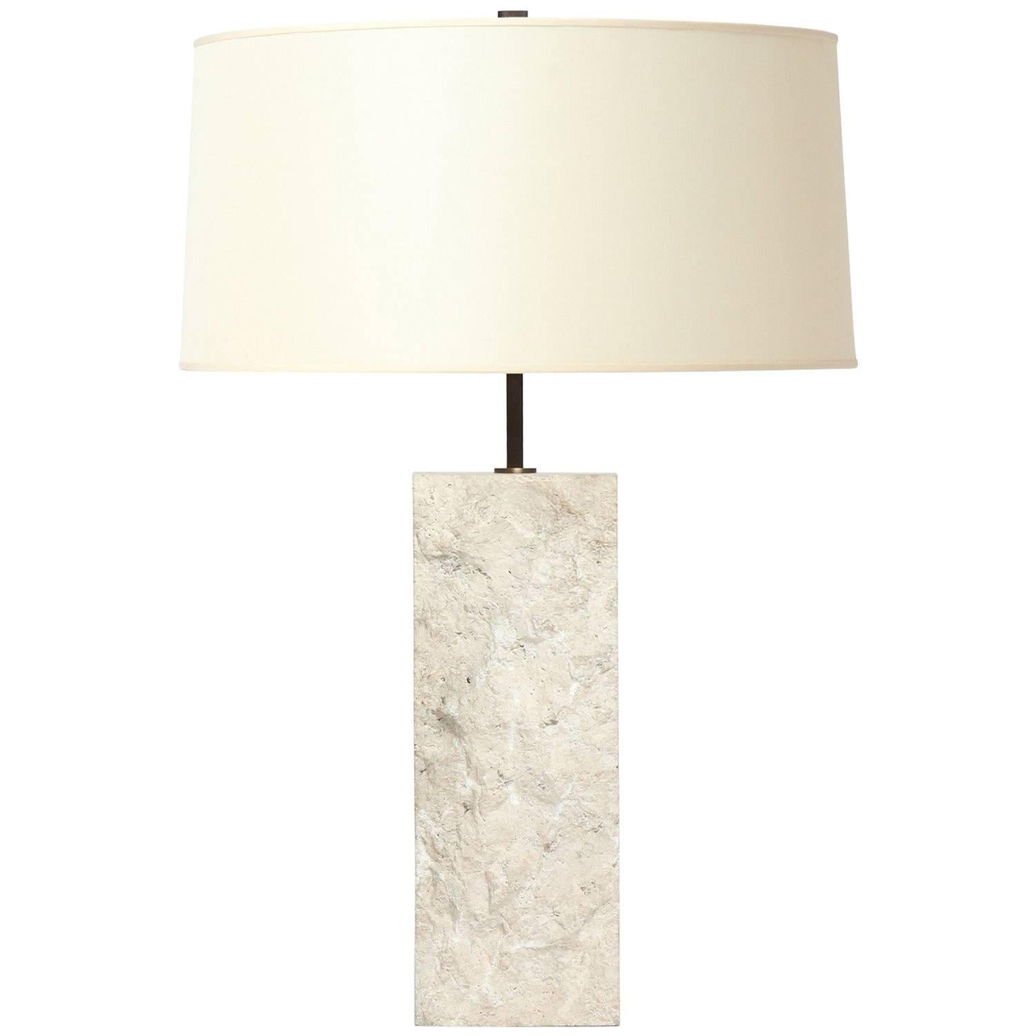 Une lampe de table rectangulaire substantielle en calcaire blanc massif avec une surface ciselée texturée.
Le corps de la lampe mesure 15.75
