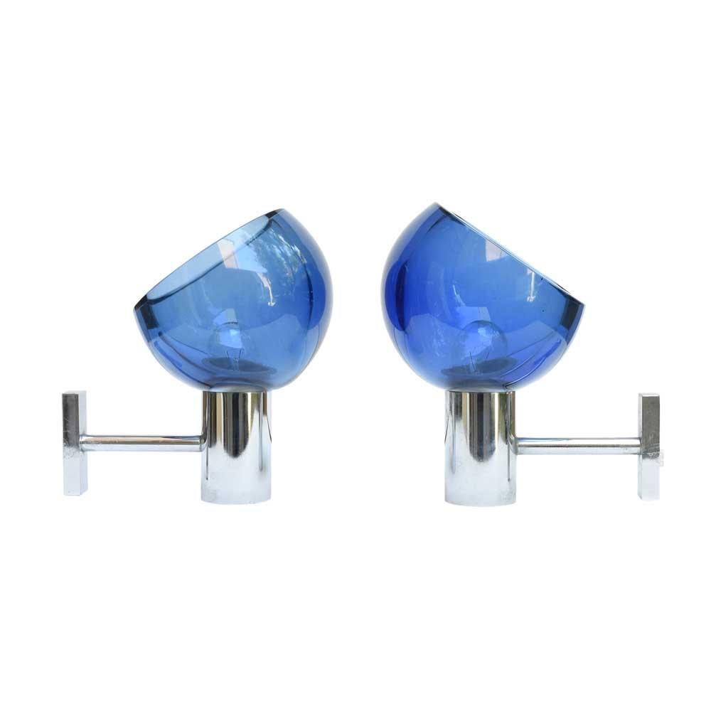 An eye-catching pair of 1960s modernist wall lights with chromed metal structures, these are elegant and functional. The transparent blue blown glass shades are spherical and create a lovely glow when lit up. These lights are an outstanding example