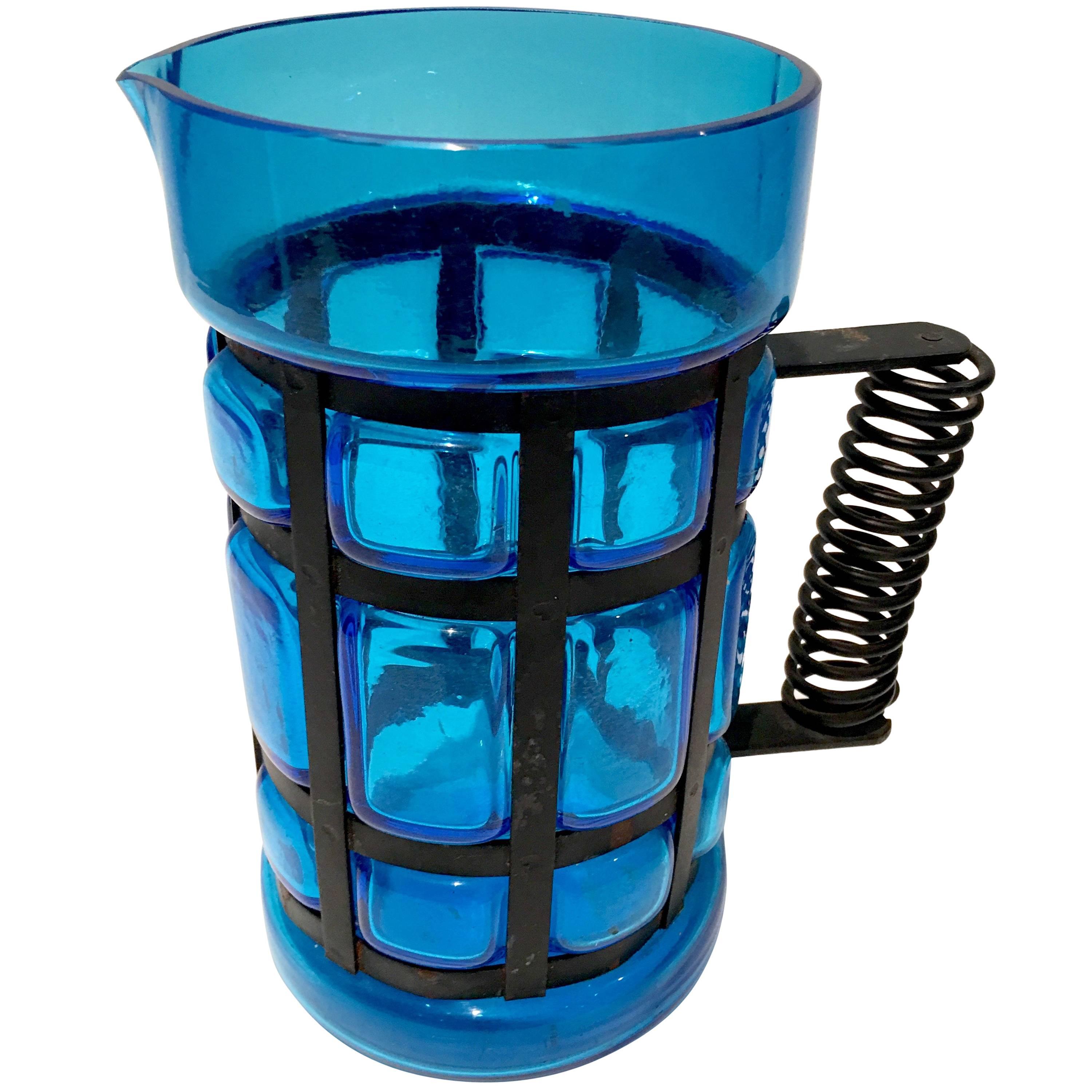Mid- 20th Century Spanish peacock blue blown glass and iron caged handled pitcher. Brilliant blue glass with black cast iron. The handle has a spiral detail and the body is pillowed. Measure: Handle, 5