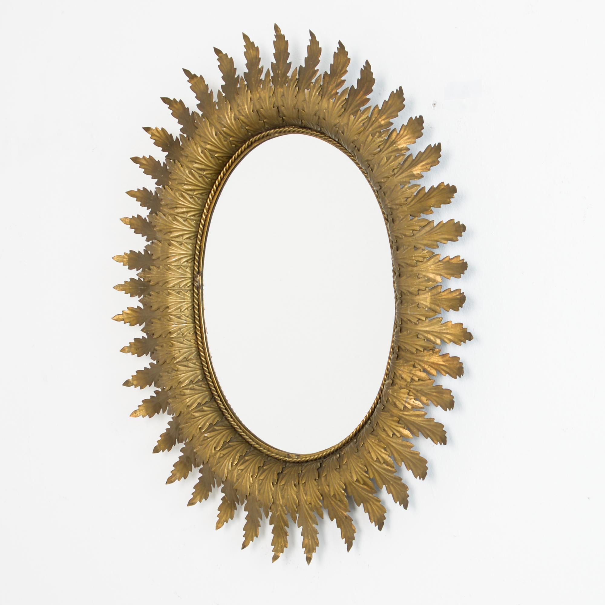 From Spain, circa 1960, an oval mirror framed by beaten metal leaves, painted with gold paint. A typical 1960s Spanish style plays on repetition, Baroque ornament, folk technique, and midcentury geometry. Chic and Bohemian accent.
  