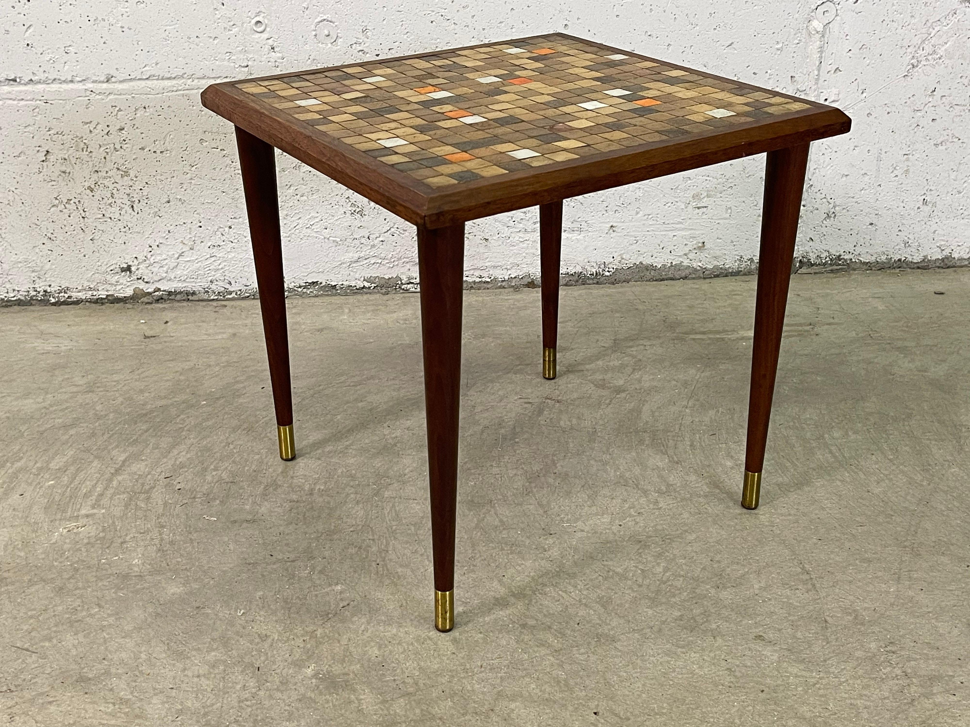 Quadratischer Beistelltisch aus den 1960er Jahren mit mehrfarbiger Kachelplatte und Nussbaumholz. Die Beine sind mit einem Messingakzent versehen. Keine Markierungen.