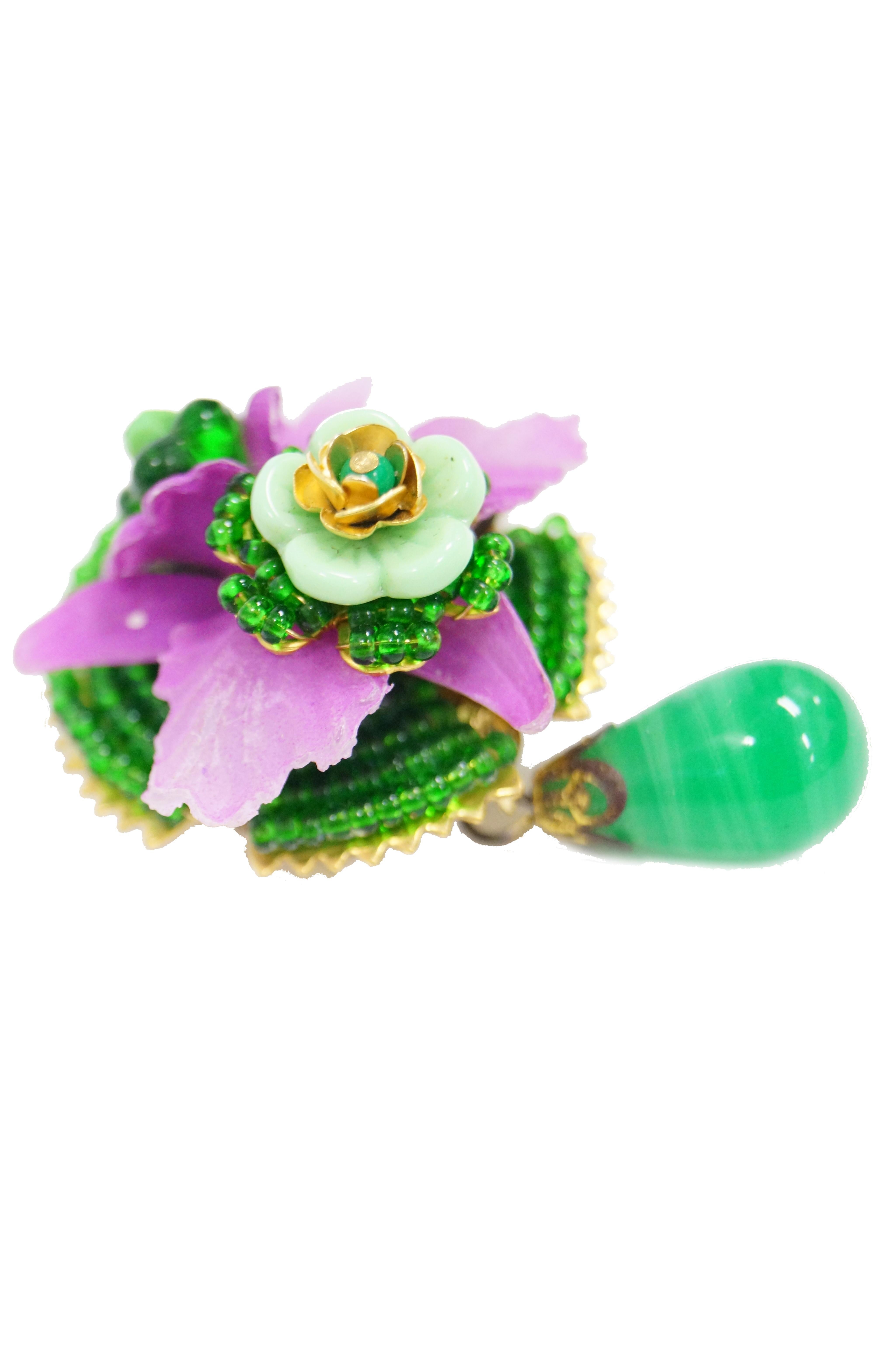 Bright and cheery floral brooch by Stanley Hagler! This intricate floral brooch is composed of a bright green glass bead base supporting a frosted purple orchid upon which lay two more green and gold beaded flowers. The body of the brooch is