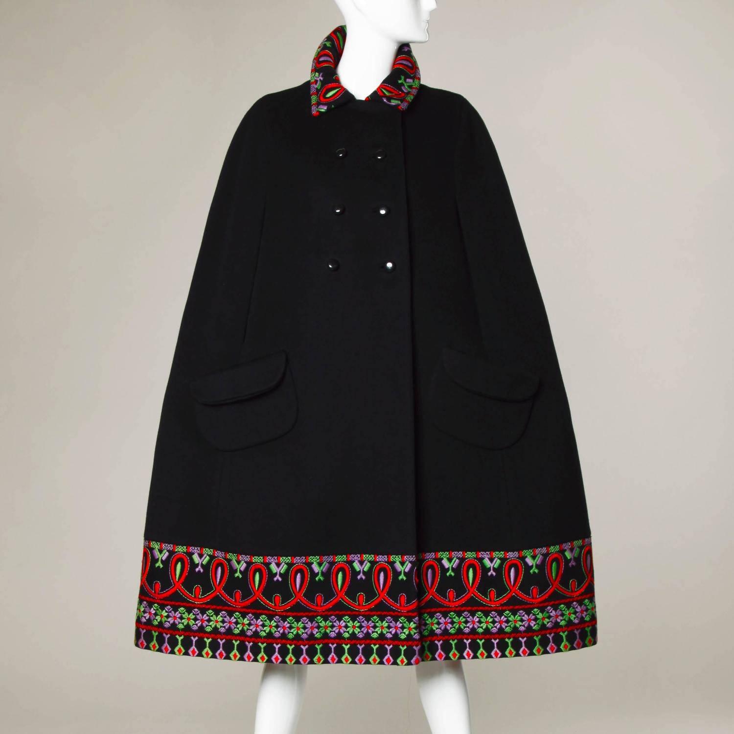 Vintage 1960s heavy black wool cape coat with folkloric-style hand embroidery, arm slits and double breasted buttons by Stegari. Fully lined in red satin with button and snap closure. Front pockets. 100% Pure virgin wool. Fits most sizes small,