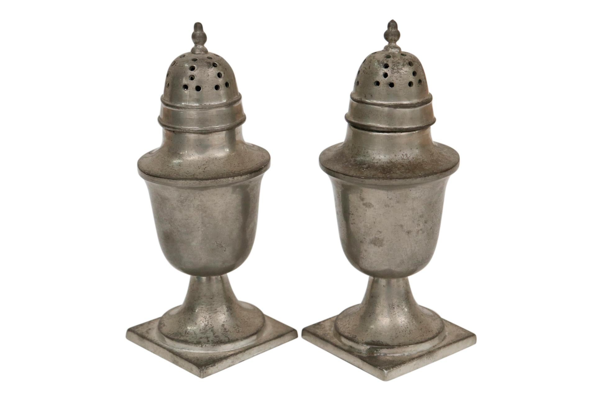 A pair of Colonial style Williamsburg Reproduction salt and pepper shakers. Manufactured by Steiff in the early 1960’s of lead free pewter. Traditional tall urns have finial topped pierced lids and square bases. Marked underneath. Dimensions per