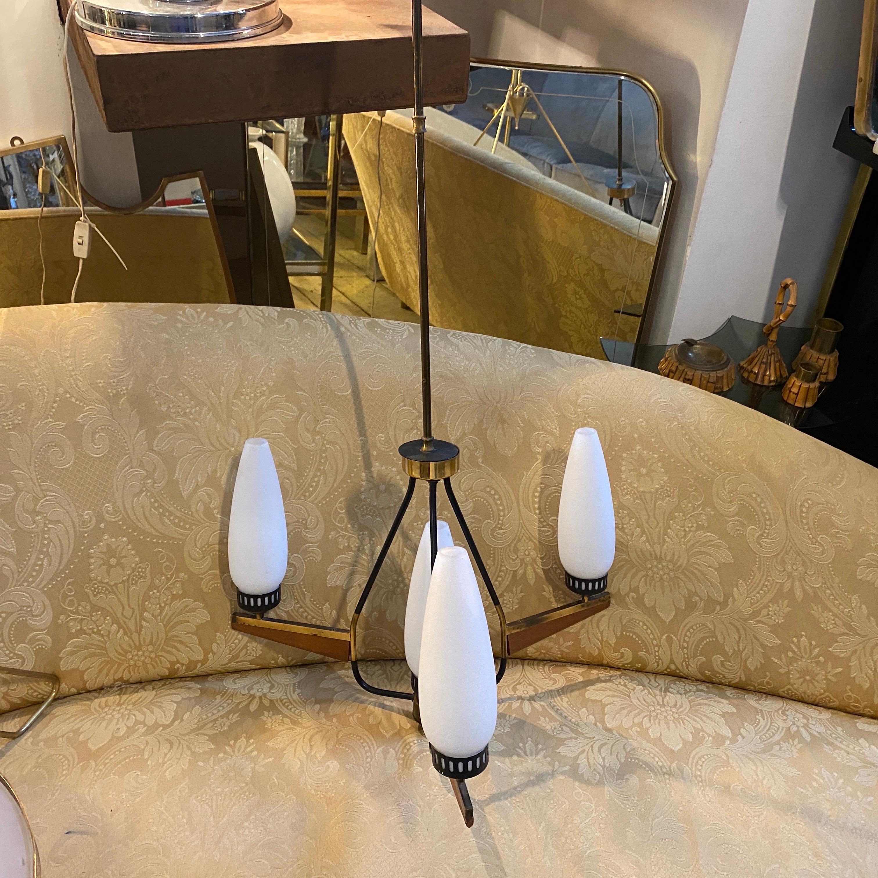 An elegant mid-century modern teak, brass and opaline glass four lights chandelier designed and manufactured in Italy in the Sixties. It's in lovely conditions, it works both 110-240 volts and needs regular e14 bulbs.
This mid-century modern