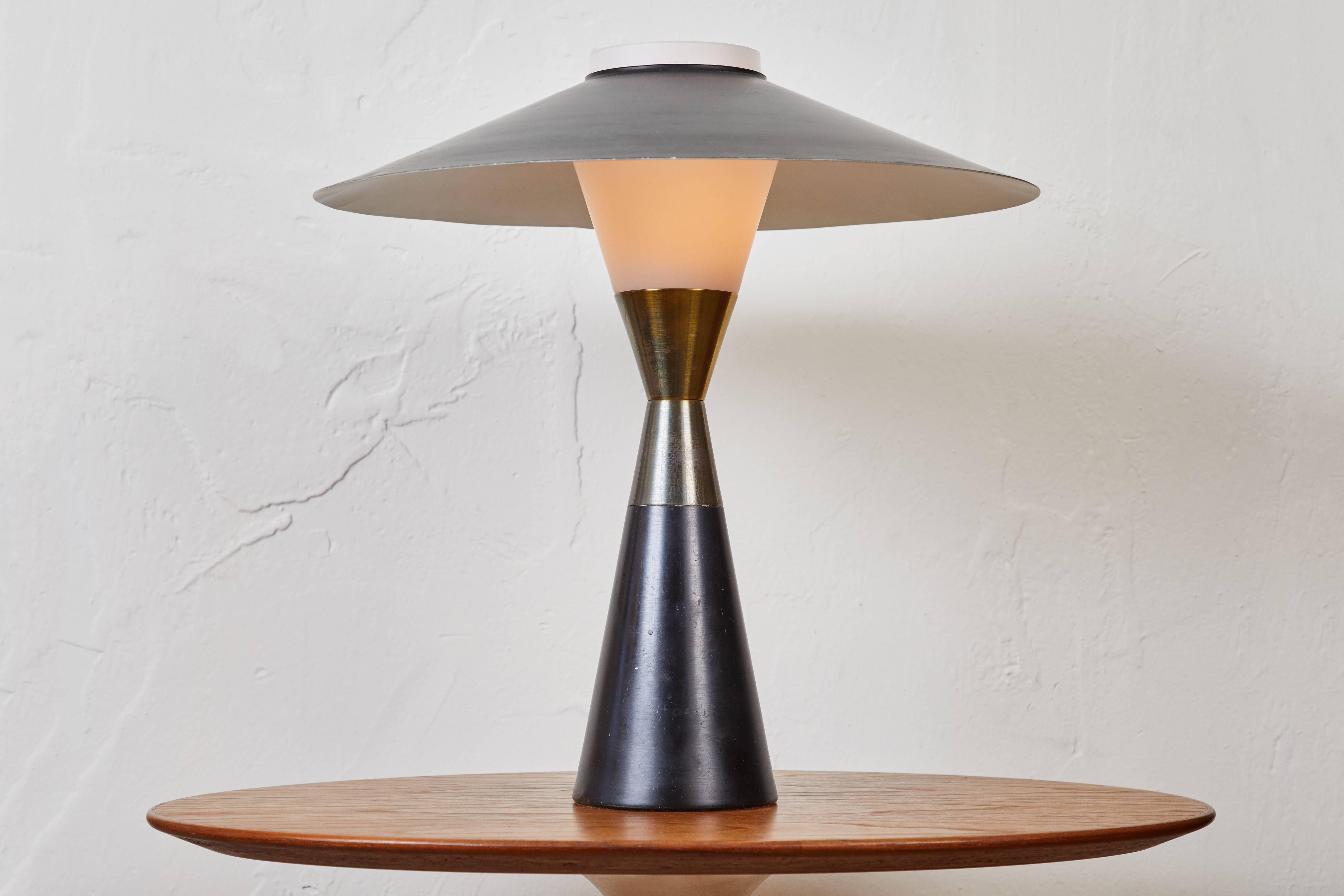 1950s Stilnovo table lamp. Executed in opaline matte glass, patinated brass and black painted metal with delicately shaped shade that rests on the glass. A sculptural and refined set of sconces characteristic of 1960s Italian design at its highest