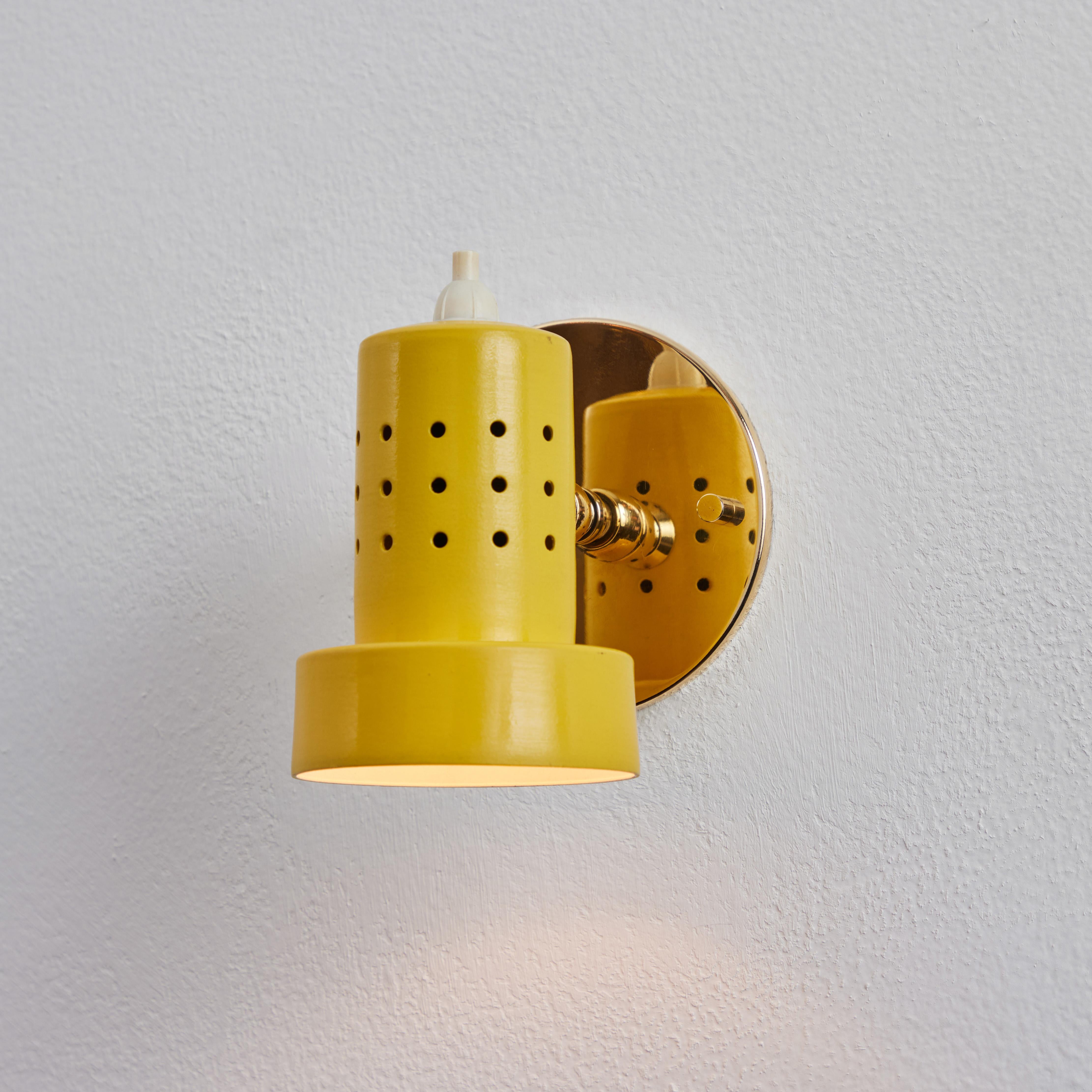 1960s Stilux Milano perforated yellow articulating sconce. Executed in brass and yellow painted metal. These highly adjustable sconces pivot up/down and rotate left/right on a ball joint. Wired for US electrical with custom period style brass