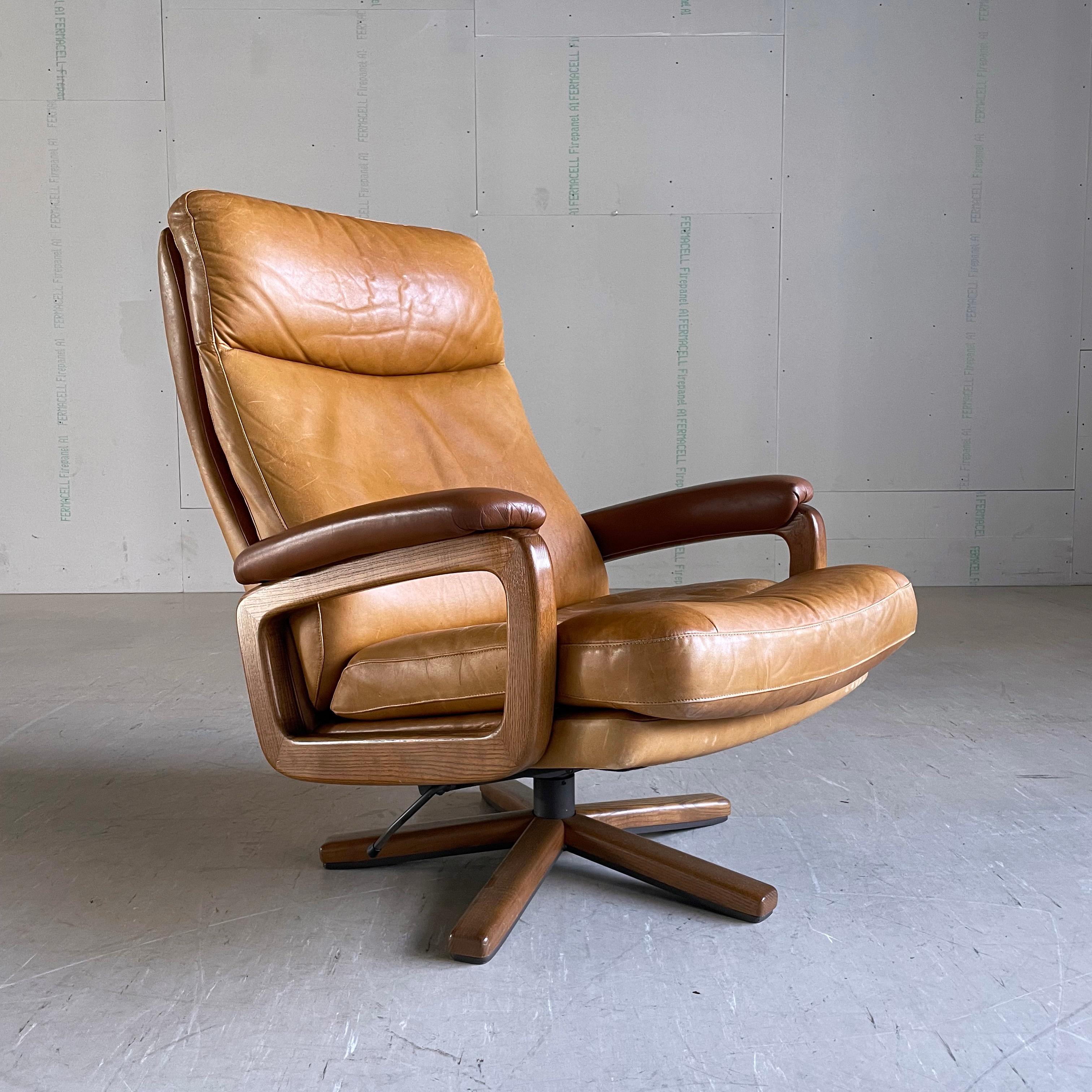 1960’s Reclining leather Lounge Chair in tanned leather. Oak swivel base and arms. Designed by André Vandenbeuck and produced by Strässle, Switzerland.
Measurements: Height: 80 cm  Width: 78cm  Depth: 70cm  Seat Height: ca. 40cm.
Both the leather