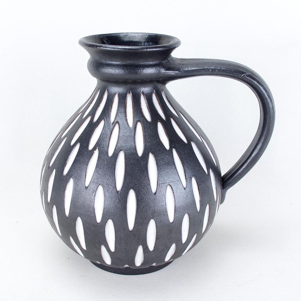Vaso in ceramica con uno smalto scuro opaco e un motivo bianco crema inciso. La brocca è stata realizzata negli anni '60 nel laboratorio di ceramica tedesco di Wilhelm & Elly Kuch. Il logo della ceramica è impresso sulla base.
Ottime condizioni e
