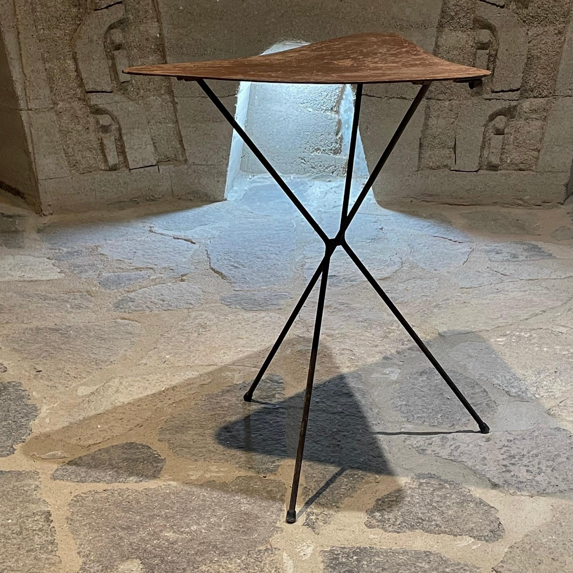 1960s stylish hipster folding tripod side table in twisted iron & sturdy faux leather laminate masonite type composite triangle top.
Unmarked.
Great design. Sturdy build. Plus ideal for compact easy storage. Clever ring to hang as shown in