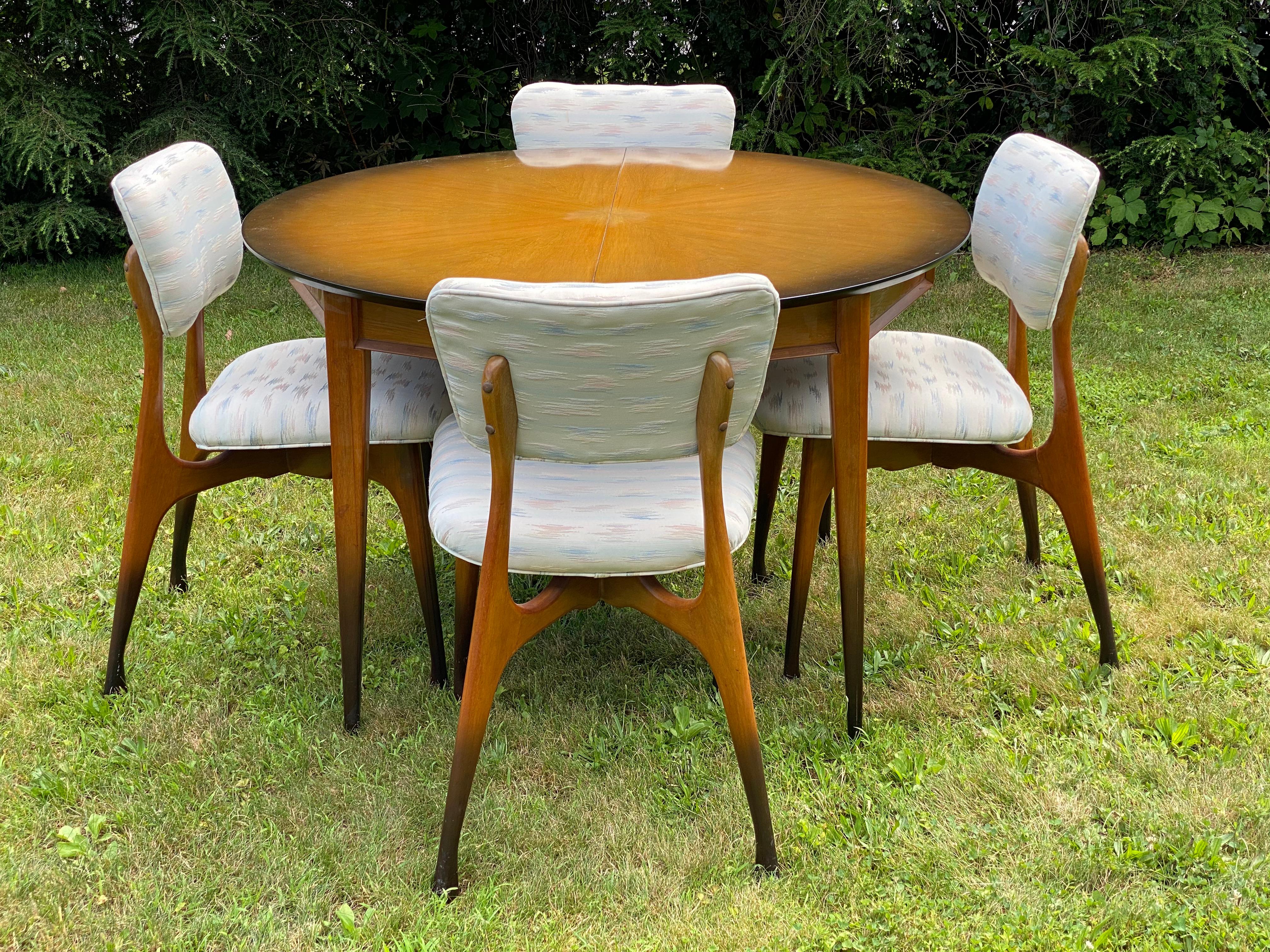 Extremely clean and well preserved dining table and chairs. Circa 1960. Featuring original sunburst finish on table and chairs. The four chairs were re-upholstered in the late 1980s. The chair frame is reminiscent of Shelby William's Gazelle chair