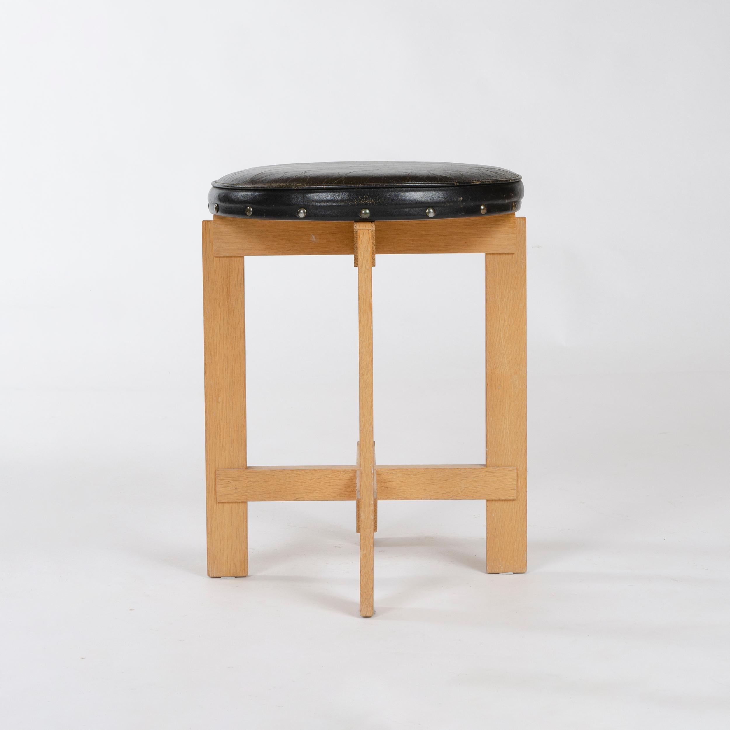A four-legged solid oak stool with X-shaped, lap-joined stretchers highlighted by their tongue and groove joinery to the legs, having a simple original leather-upholstered circular seat. Marked with original LUXUS sticker.