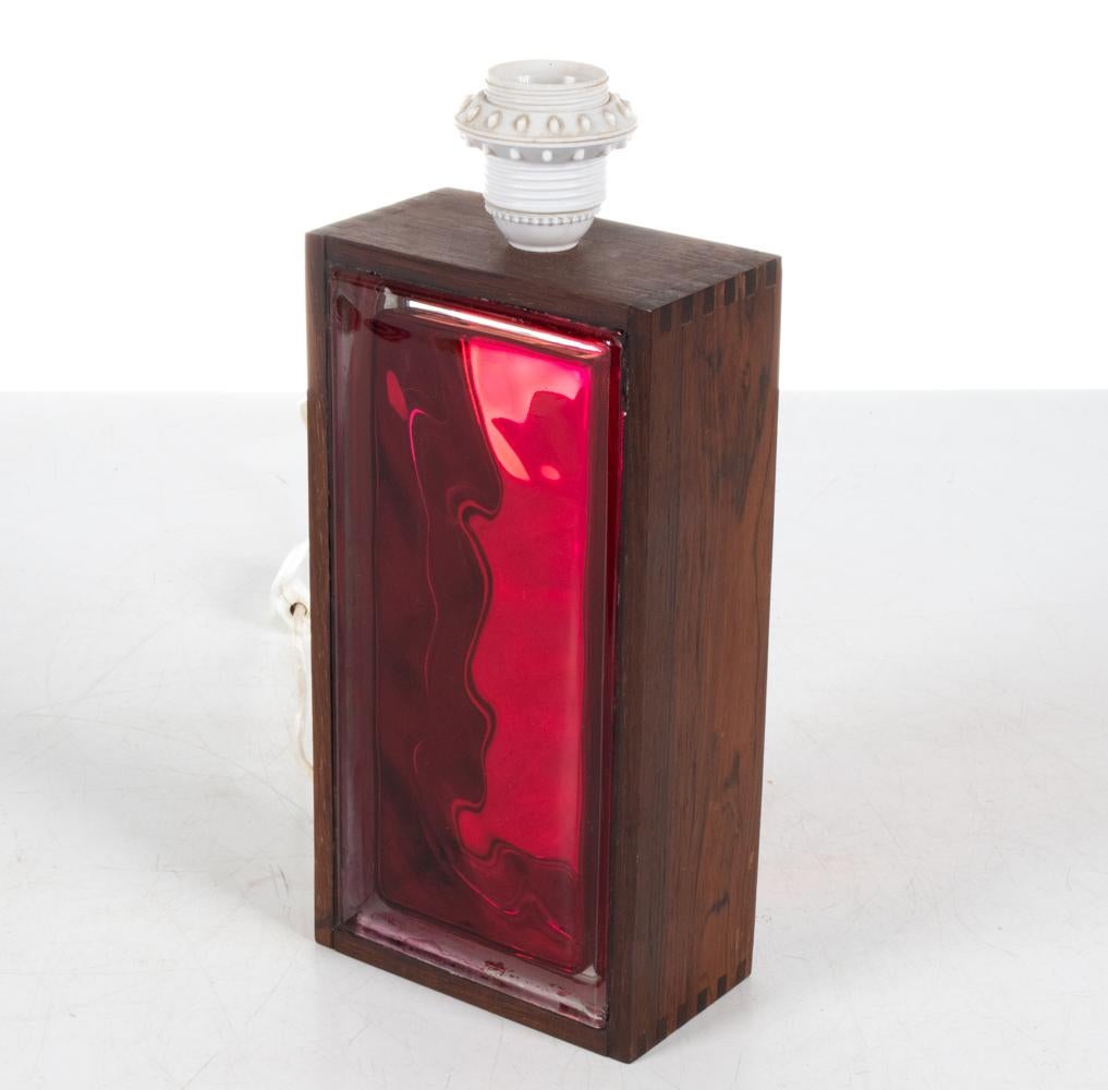 Step into the radiant world of 1960s Swedish design with this dazzling table lamp, where a fiery red glass brick seamlessly meld with the opulent depths of rosewood. An artifact of an age when design broke barriers, this lamp encapsulates the daring