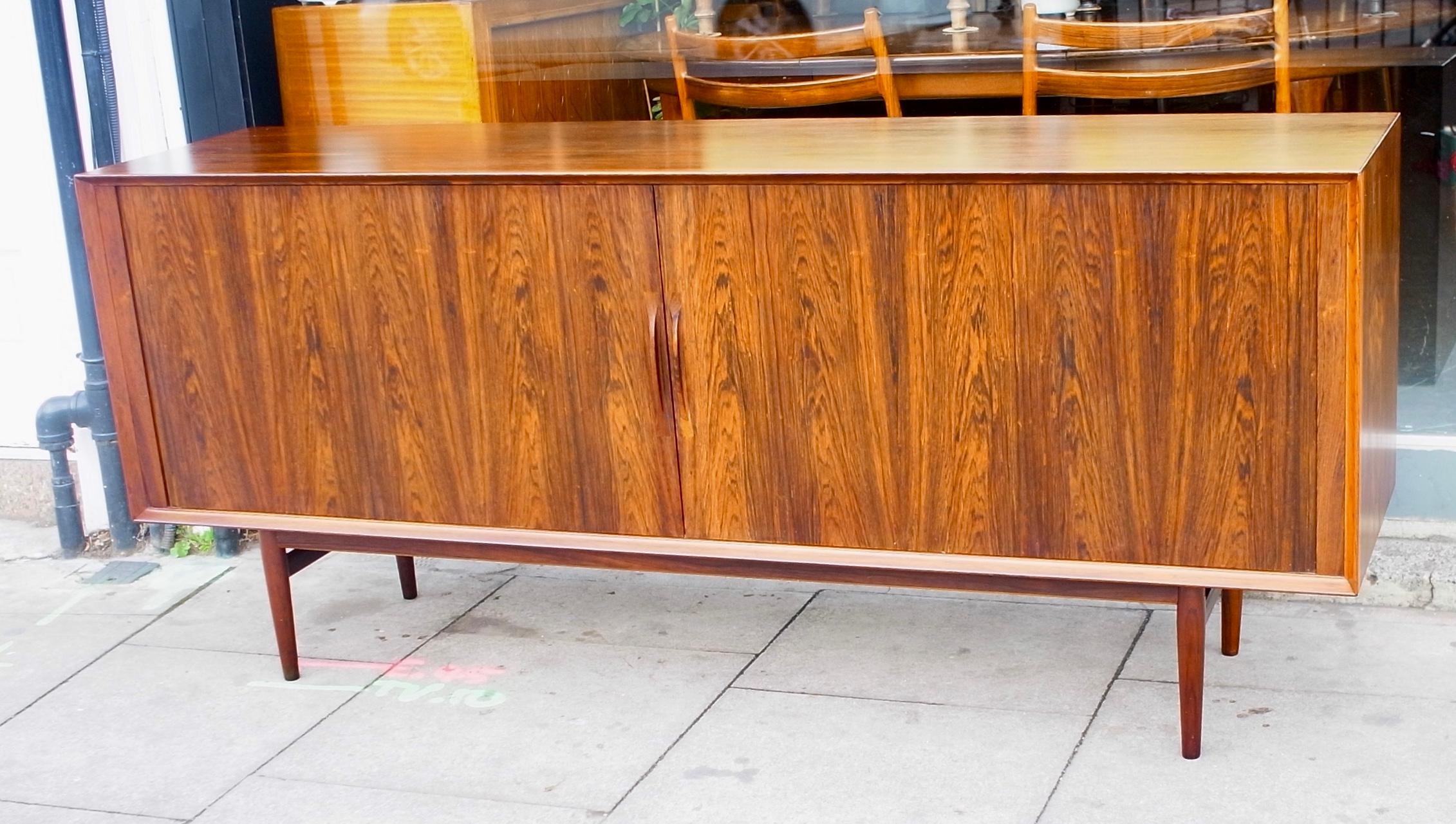 A beautiful example of a Arne Vodder designed rosewood sideboard produced by Sibast. Based on four solid rosewood turned tapered legs, this piece has two tambour fronted doors with delicately carved handles. The sycamore interior, consists of 3x