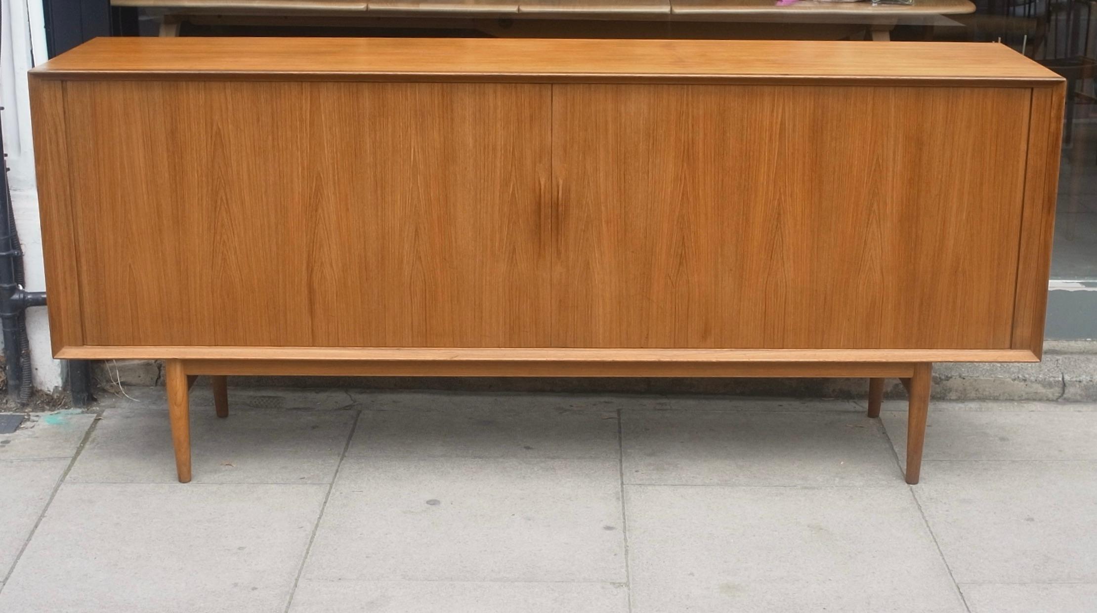 A beautiful example of a Arne Vodder designed teak sideboard produced by Sibast. Based on four solid teak turned tapered legs, this piece has two tambour fronted doors with delicately carved handles. The sycamore interior, consists of 3x centrally