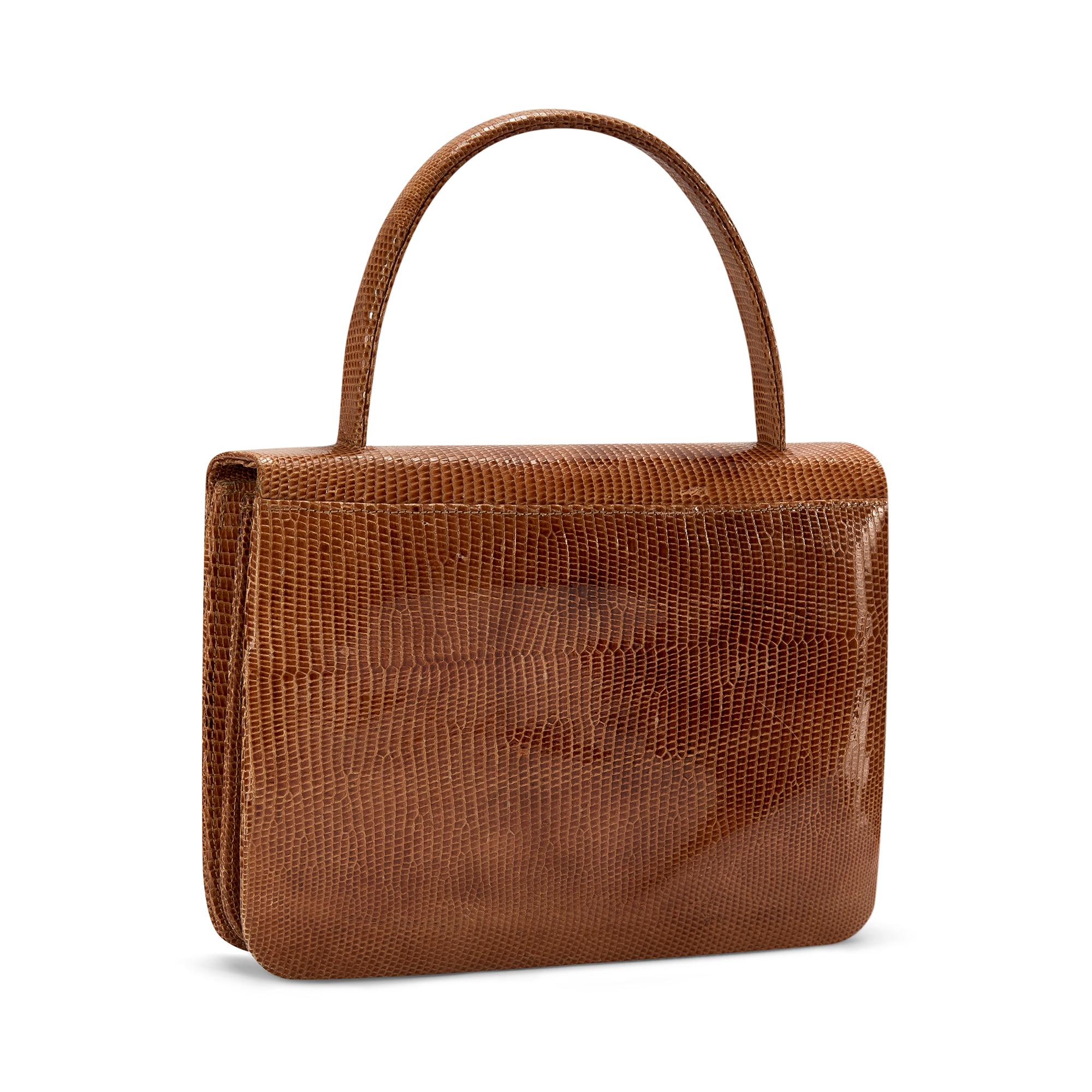 This fine quality 1960s bag is crafted from the best tan lizard leather with a short top handle and flap closure. The intricate clasp is sculpted from brass and detailed with coordinating lizard leather. Inside, there is a concertina opening with