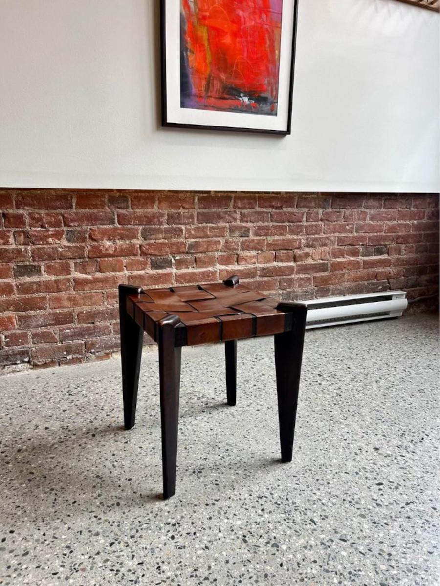 We are excited to offer this 1960s stool crafted by Edmond Spence, featuring a solid teak frame with a woven leather seat. This piece showcases a nuanced sculptural design, where simple leather and hardwood converge to create a captivating