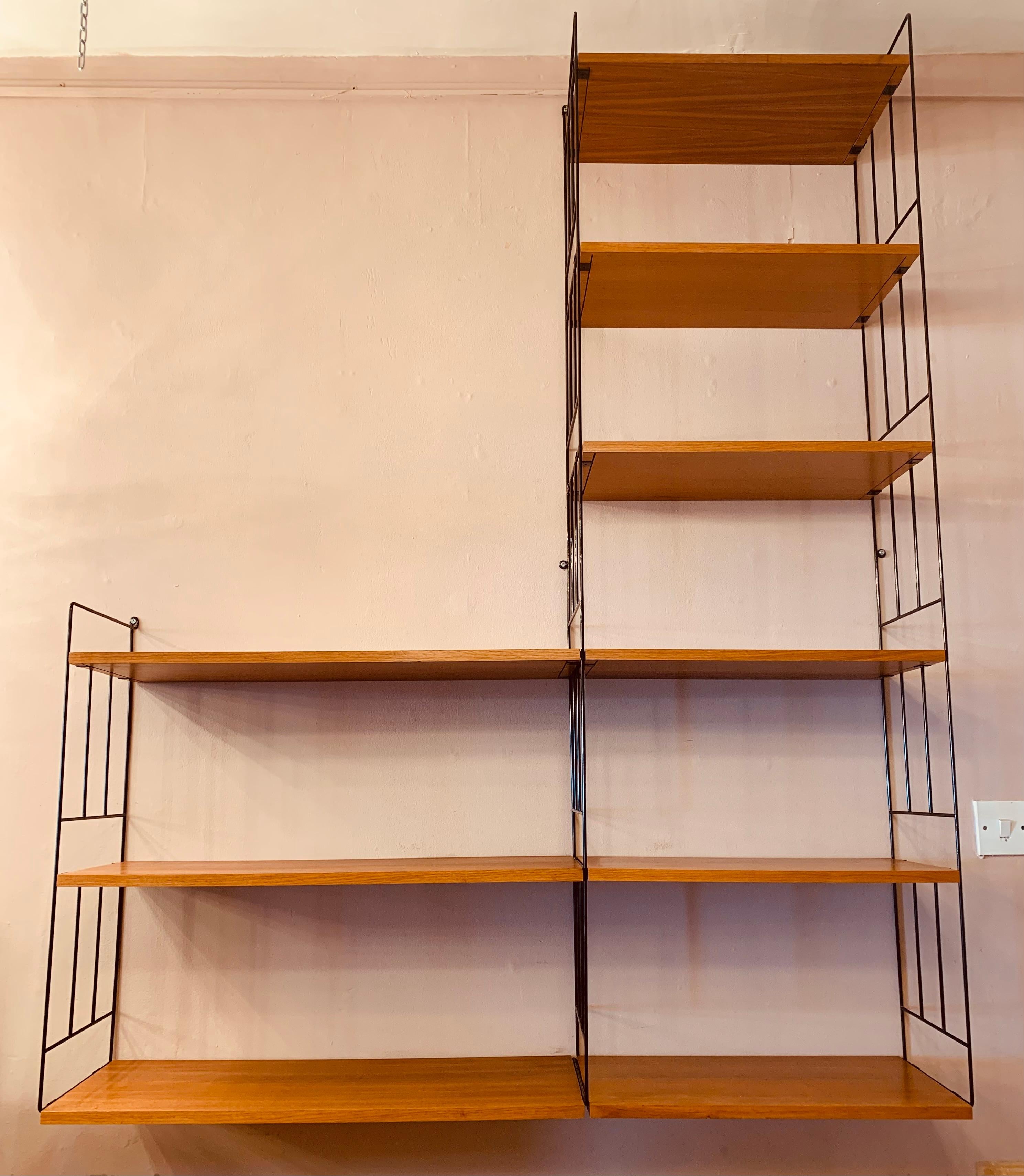 1960s, mid century, wall-mounted, hanging-ladder shelving system, produced by WHB in Germany. The system features three black metal string ladders, which are screwed into the wall to hold the Teak, veneered shelves in place, which easily clip onto