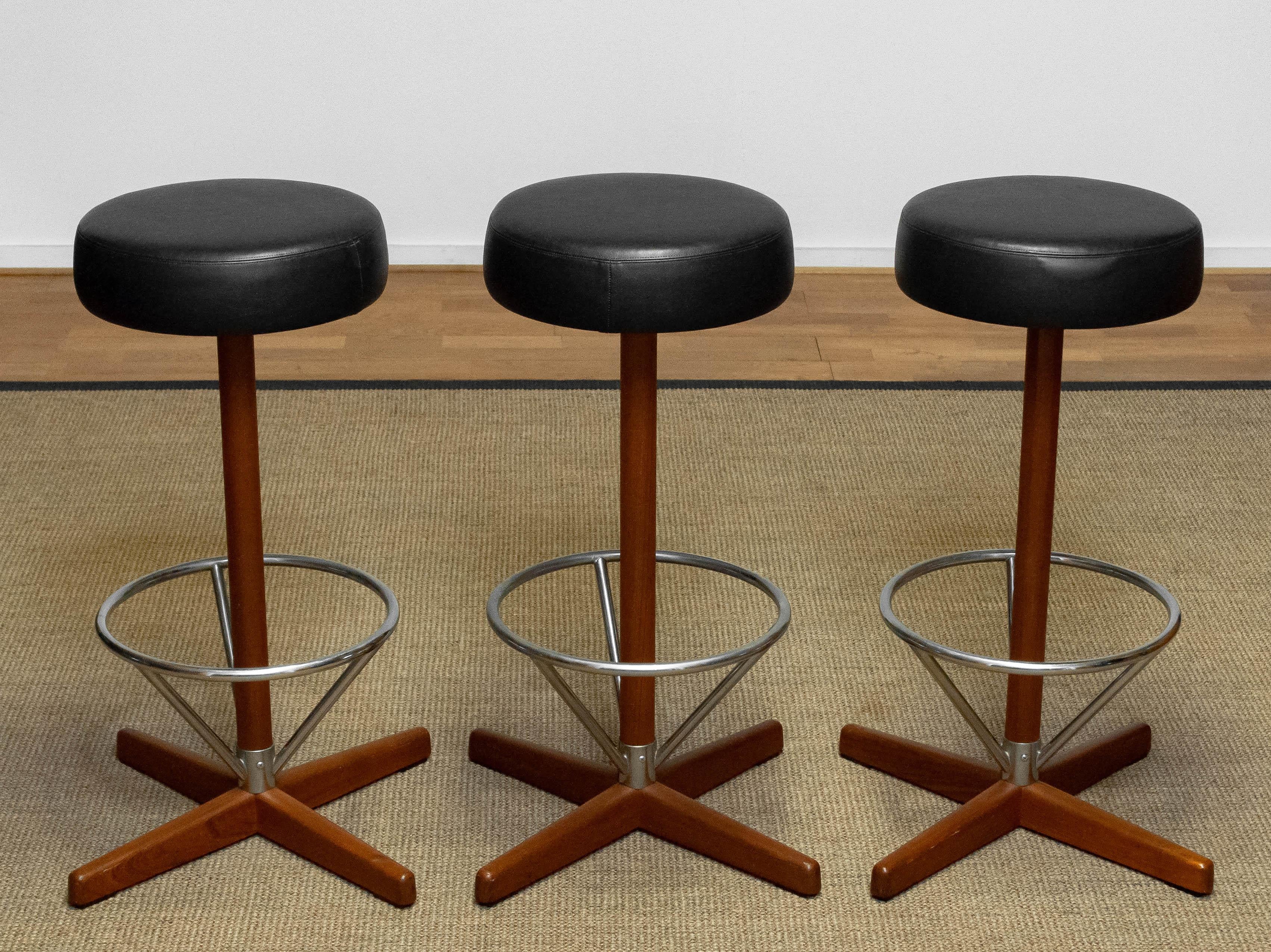 Beautiful group of three teak and chrome swivel bar stools designed by Börje Johanson for Johanson Design upholstered with black faux leather.
All three stools are in good condition.