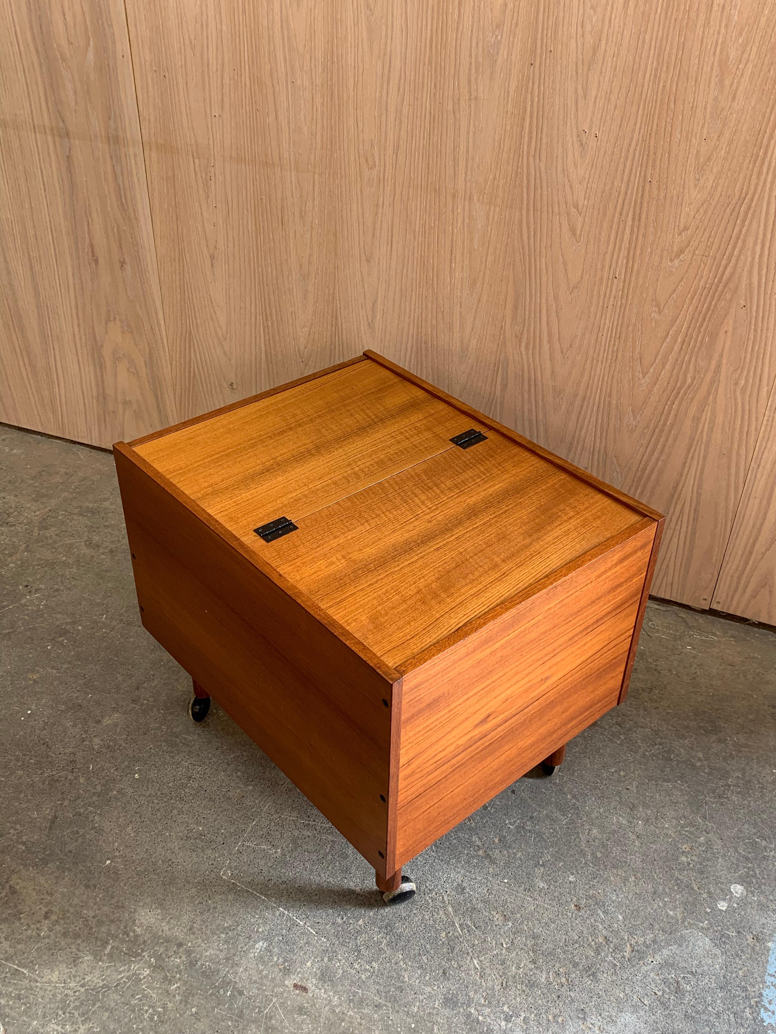 Compacta, inteligente y de bella factura. Este mueble vintage de teca tiene un frente abatible con soportes de cadena de latón, estante interior y ruedas de desplazamiento suave.

Perfecto como carrito de bar, tocadiscos, mesilla de noche o solución