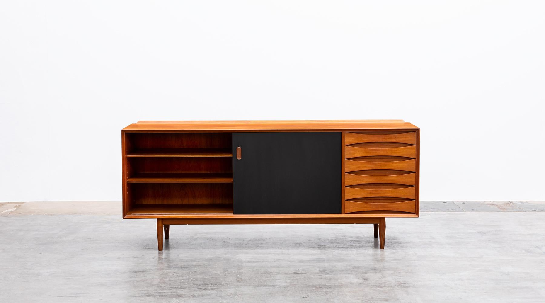 Arne Vodder sideboard with two reversible sliding doors in a teak corpus. This beautiful piece contains five drawers with concave handles. The sliding doors can be used from both sides; one side is in teak the other side is lacquered in black.