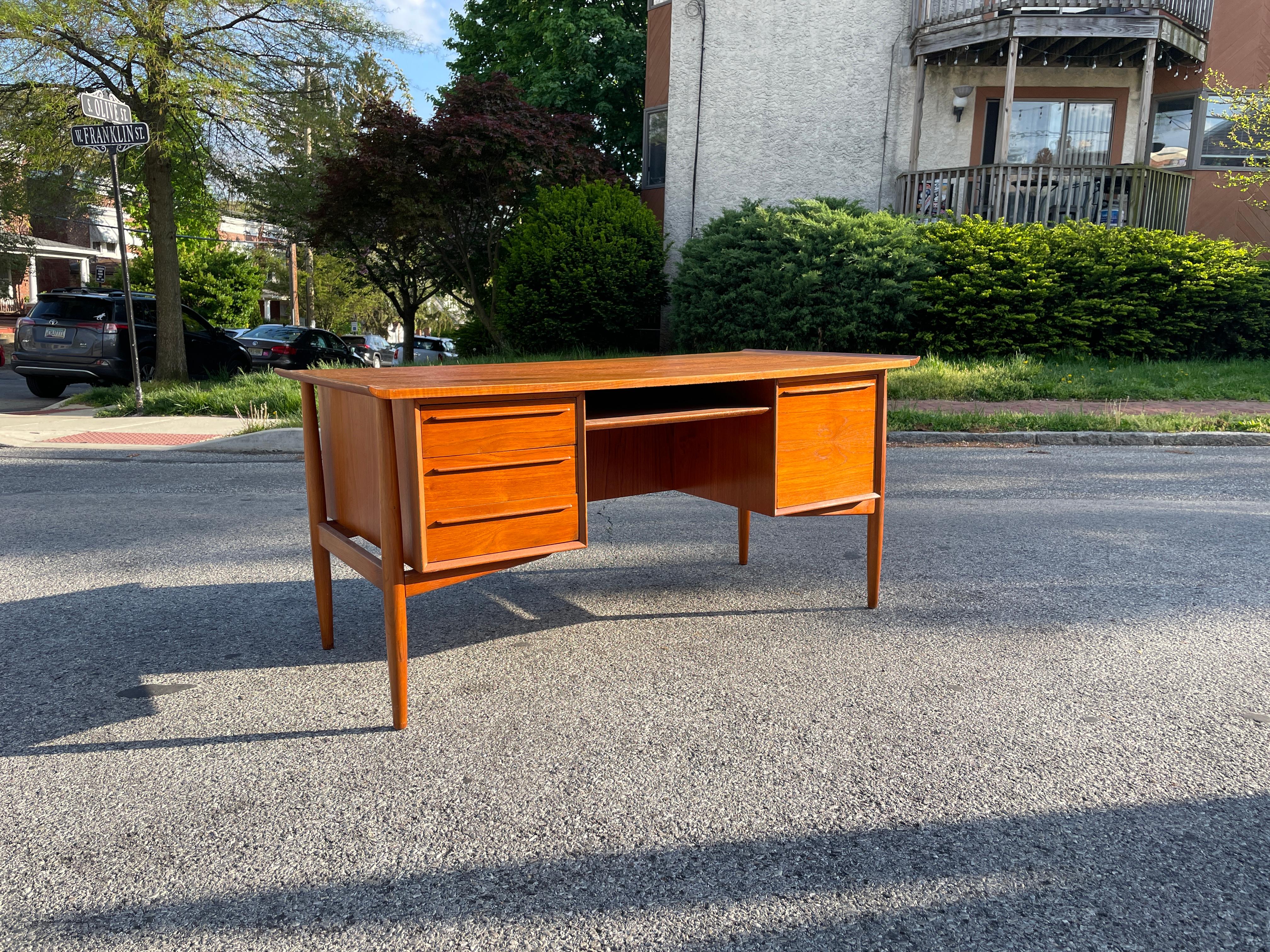 A beautiful teakwood executive desk by Arne Vodder, complete with a bookshelf and locking bar cabinet on the back. The front of the desk has three drawers, one large drawer cabinet, and a cubby slot perfect for storing a keyboard. The top has sleek