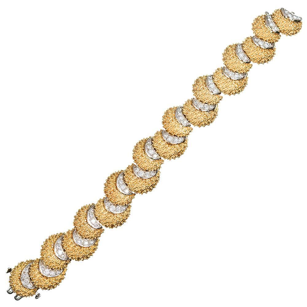 Dappled links of 18 karat yellow gold are spaced with diamond-studded crescent moon-shaped motifs of 18 karat white gold. The yellow gold sections are reminiscent of seashells and exude ample mid-century charm. The bracelet measures 7 inches long