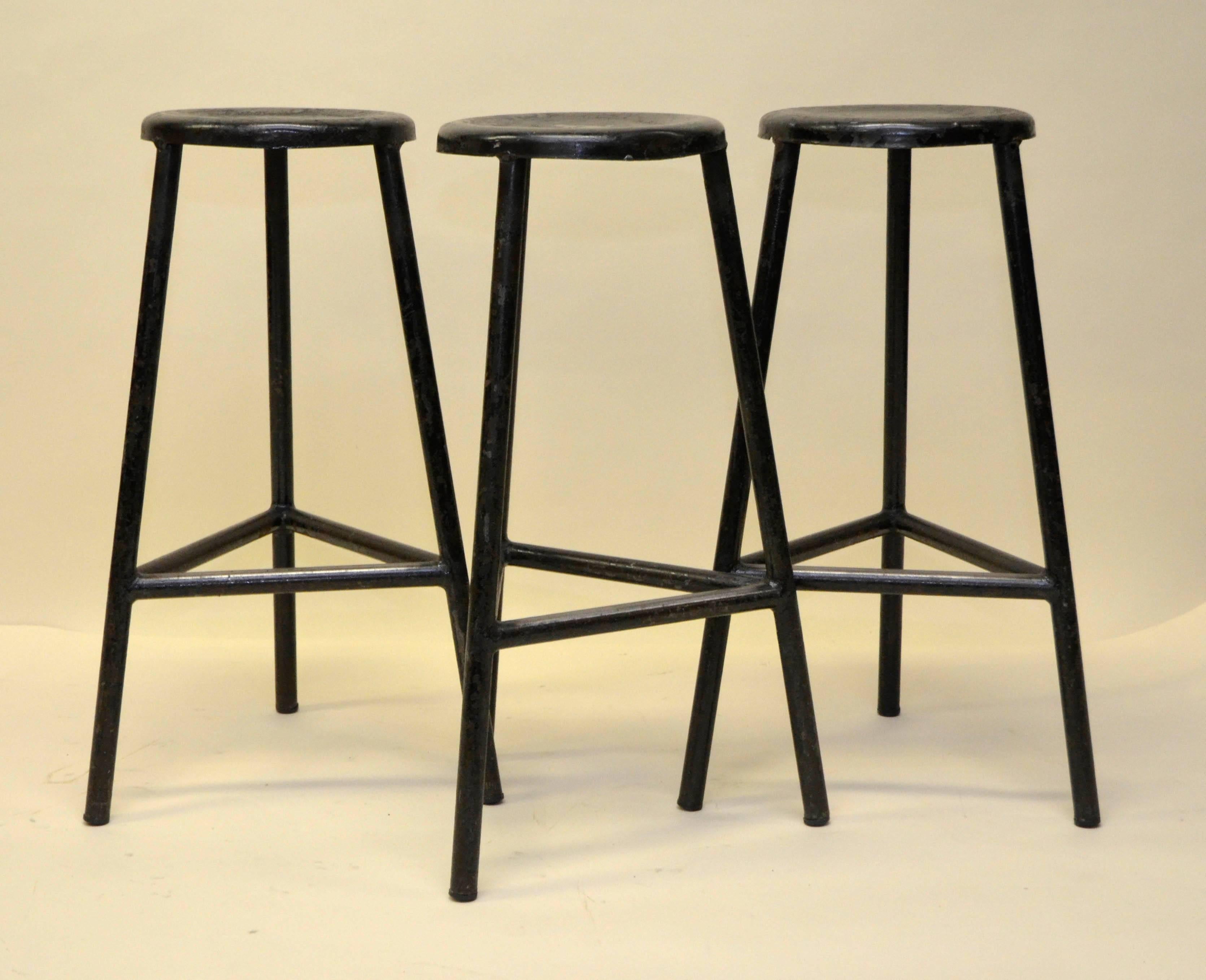 Three black metal 1960s Italian industrial design three-legged bar high stools with comfortable foot rail.
Measures: Seat height 70 cm, round seat diameter 42 cm.
Triangular shaped foot rail height 27 cm.

Two set of three in stock.