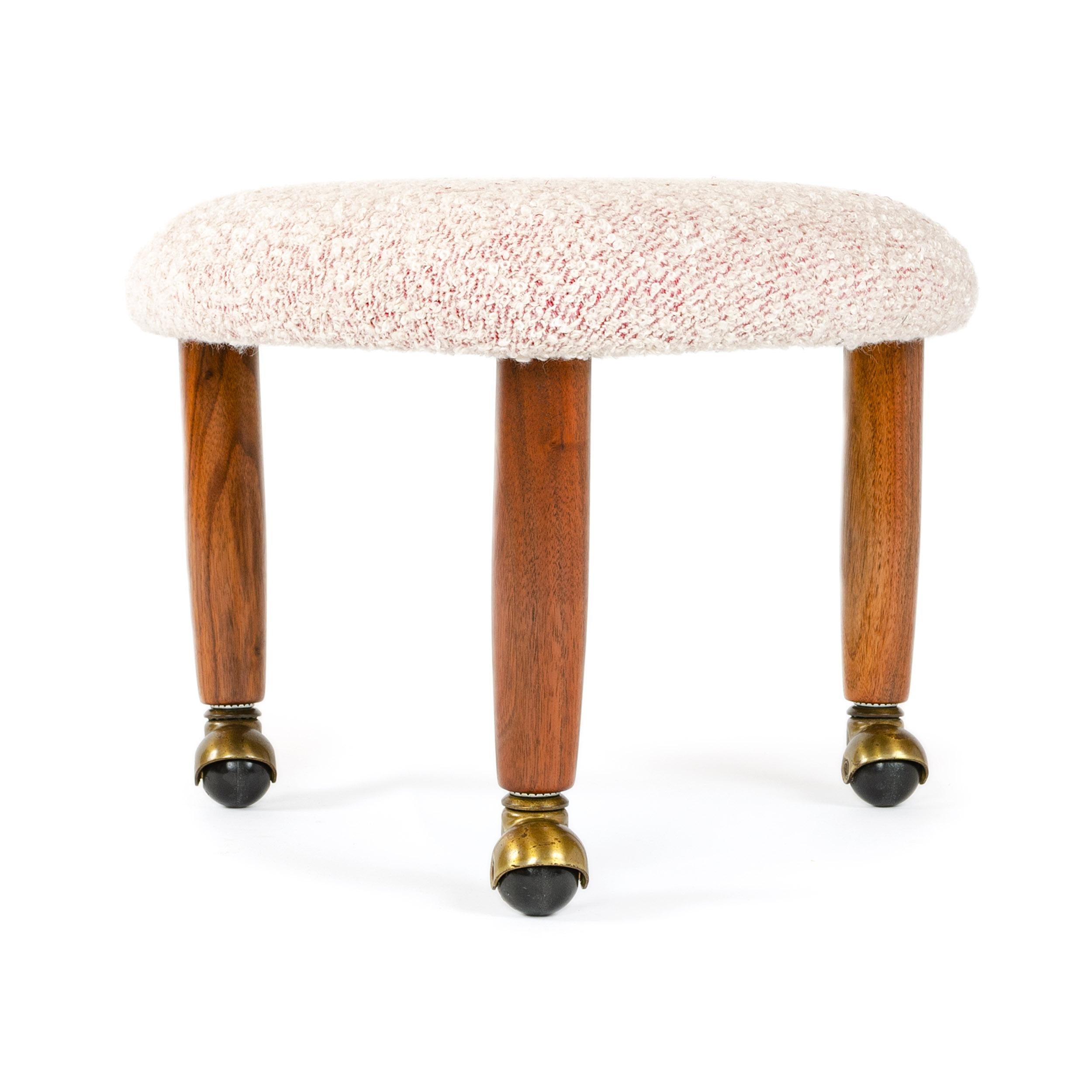 A newly upholstered three (3) legged triangular stool in raspberry boucle on swollen dowel legs with caster feet.