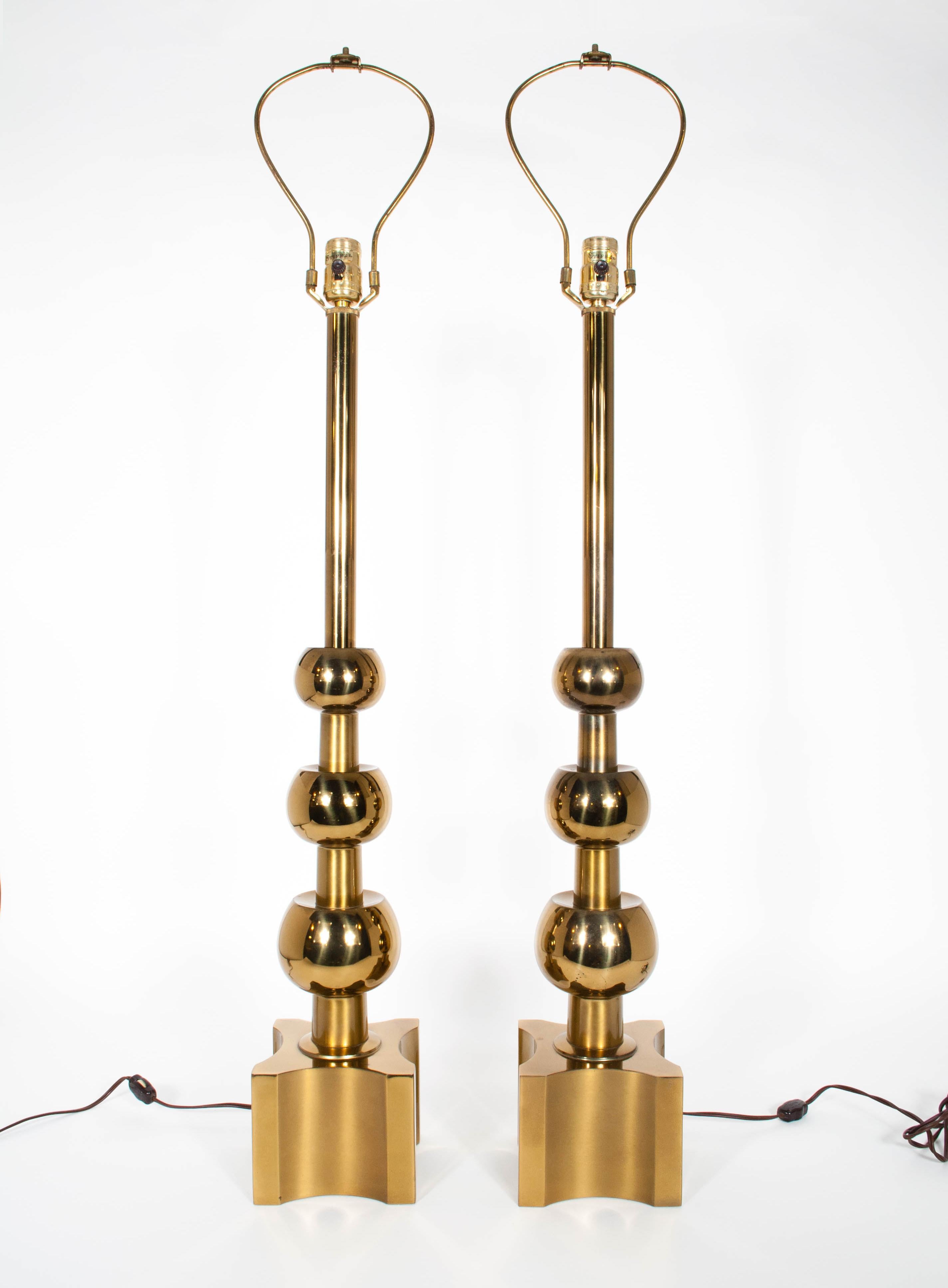 Iconic pair of midcentury brass lamps by Tommi Parzinger for Stiffel Lamp Company. The glamorous and grand lamps feature a stepped three-ball design and an X-block base. Original paper labels are present on the socket of each lamp. Monumental in