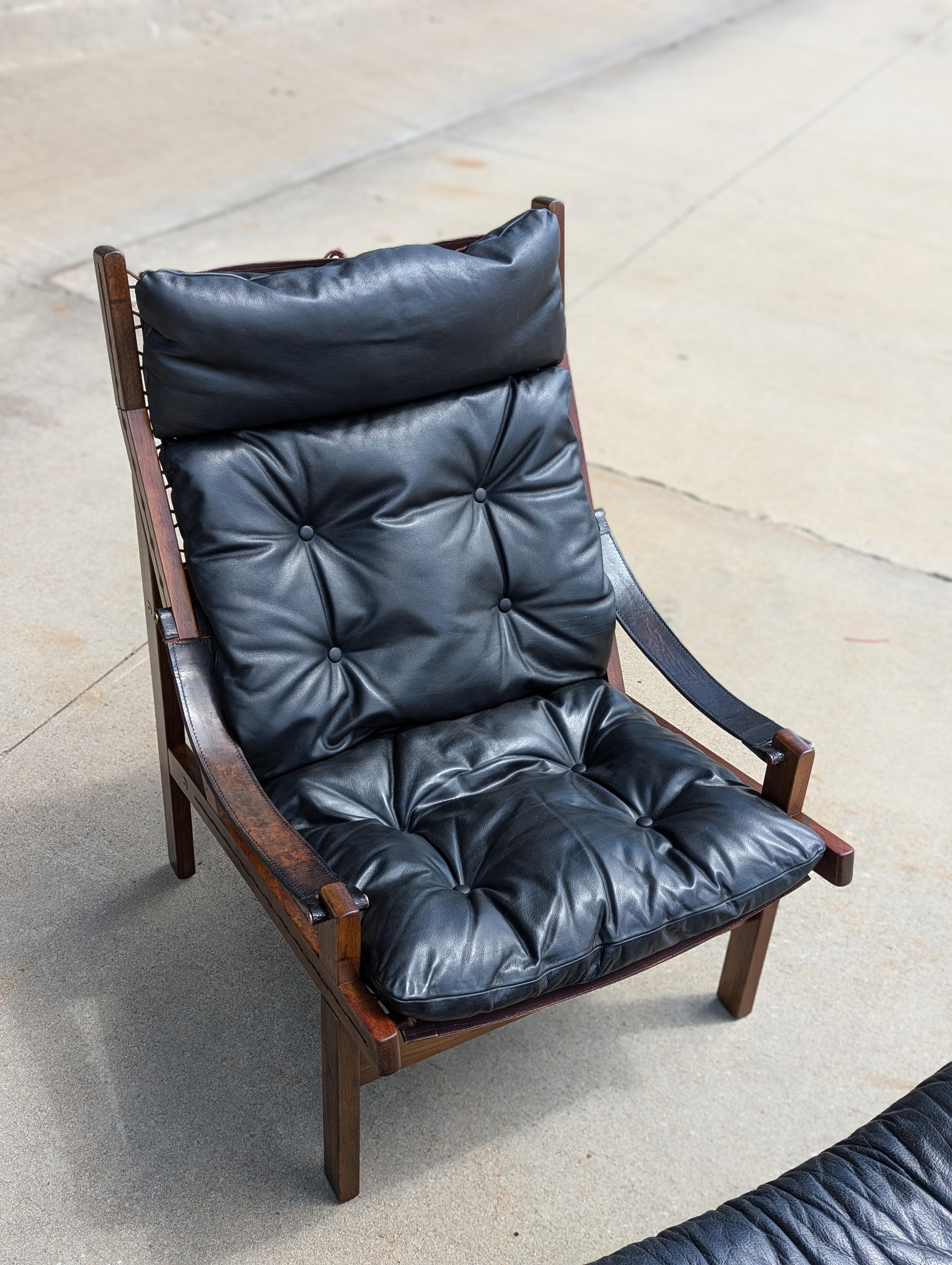 Hunter safari lounge chair and matching footstool by Torbjørn Afdal for Bruksbo, Norway. Circa 1960s.

Solid rosewood frame, brass pins, original black leather cushion and arm rest straps.

Good vintage condition, very comfortable.
