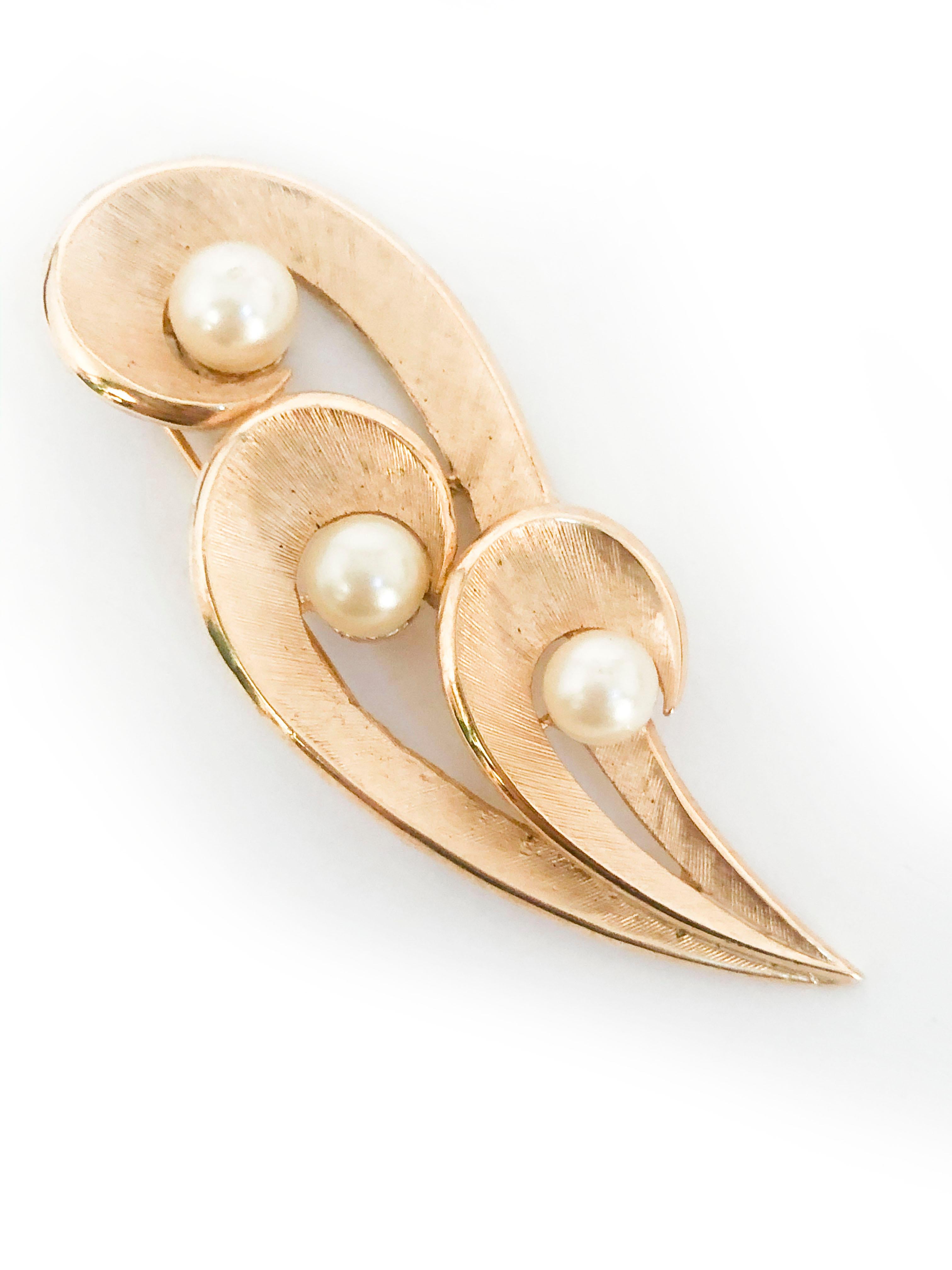 1960s Trifari brooch featuring textured and finished brass curve-like shapes centered with three glass pearls. The back has a standard brooch pin and hallmarked with 