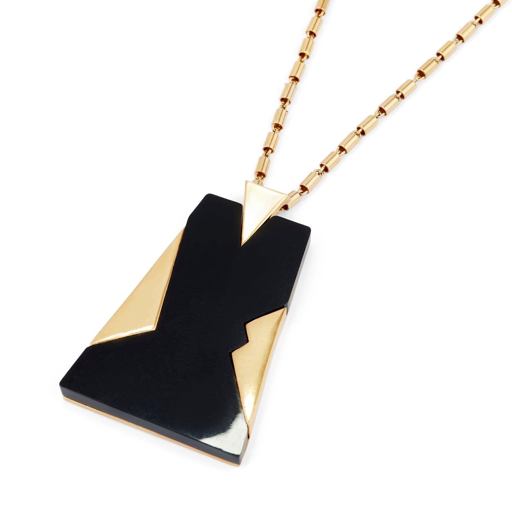 Questa straordinaria collana con ciondolo è firmata Trifari. Composta da una lunga catena dorata e da un grosso ciondolo, questa collana è stata disegnata alla fine degli anni Sessanta. Il ciondolo è realizzato in plastica nera lucida, interrotta da