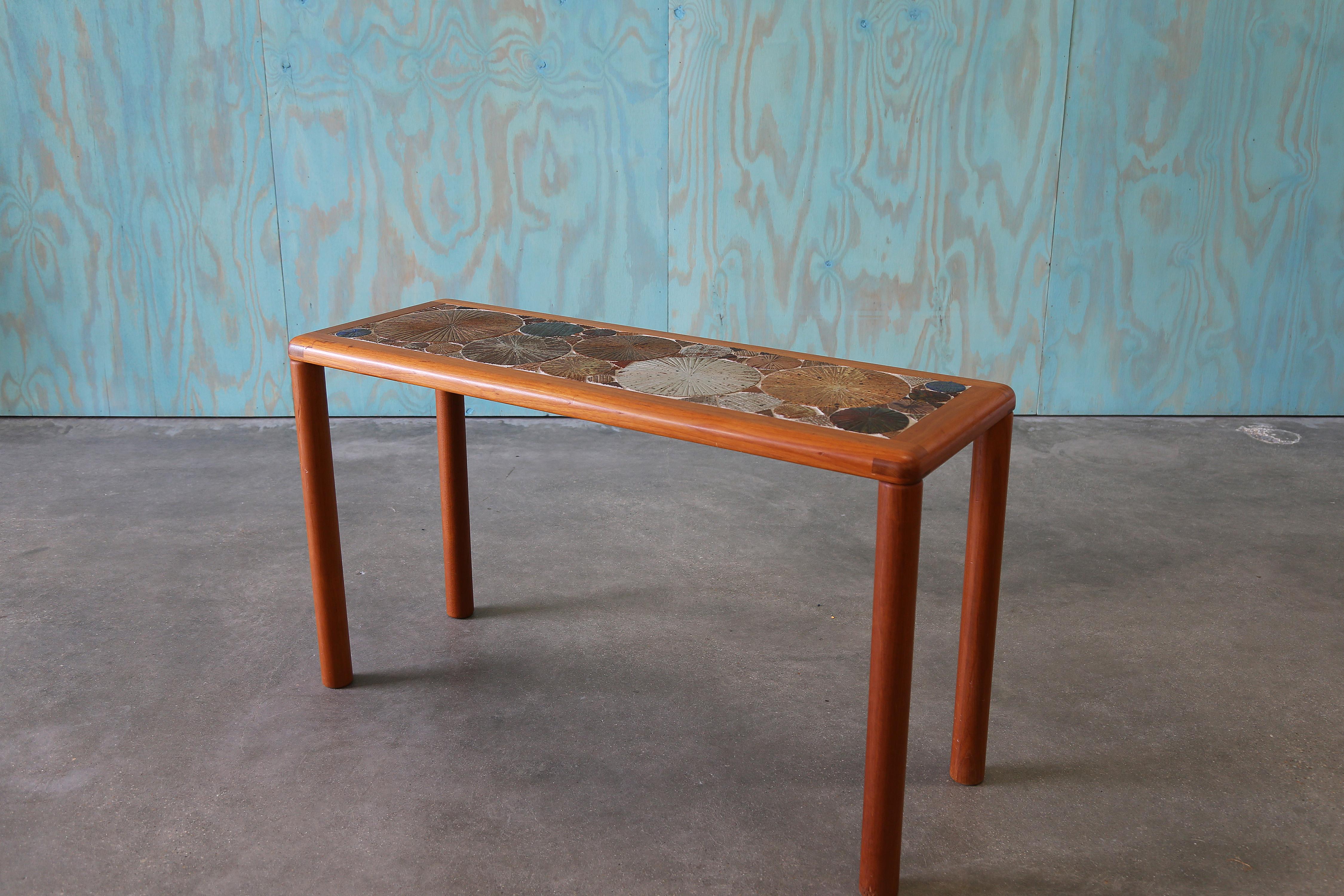 An exceptional example of Danish mid-century craftsmanship, this console table was designed by renowned artist Tue Poulsen for Haslev Møbelsnedkeri A/S in 1960. The piece features a richly stained teak frame with a sculptural rim, showcasing