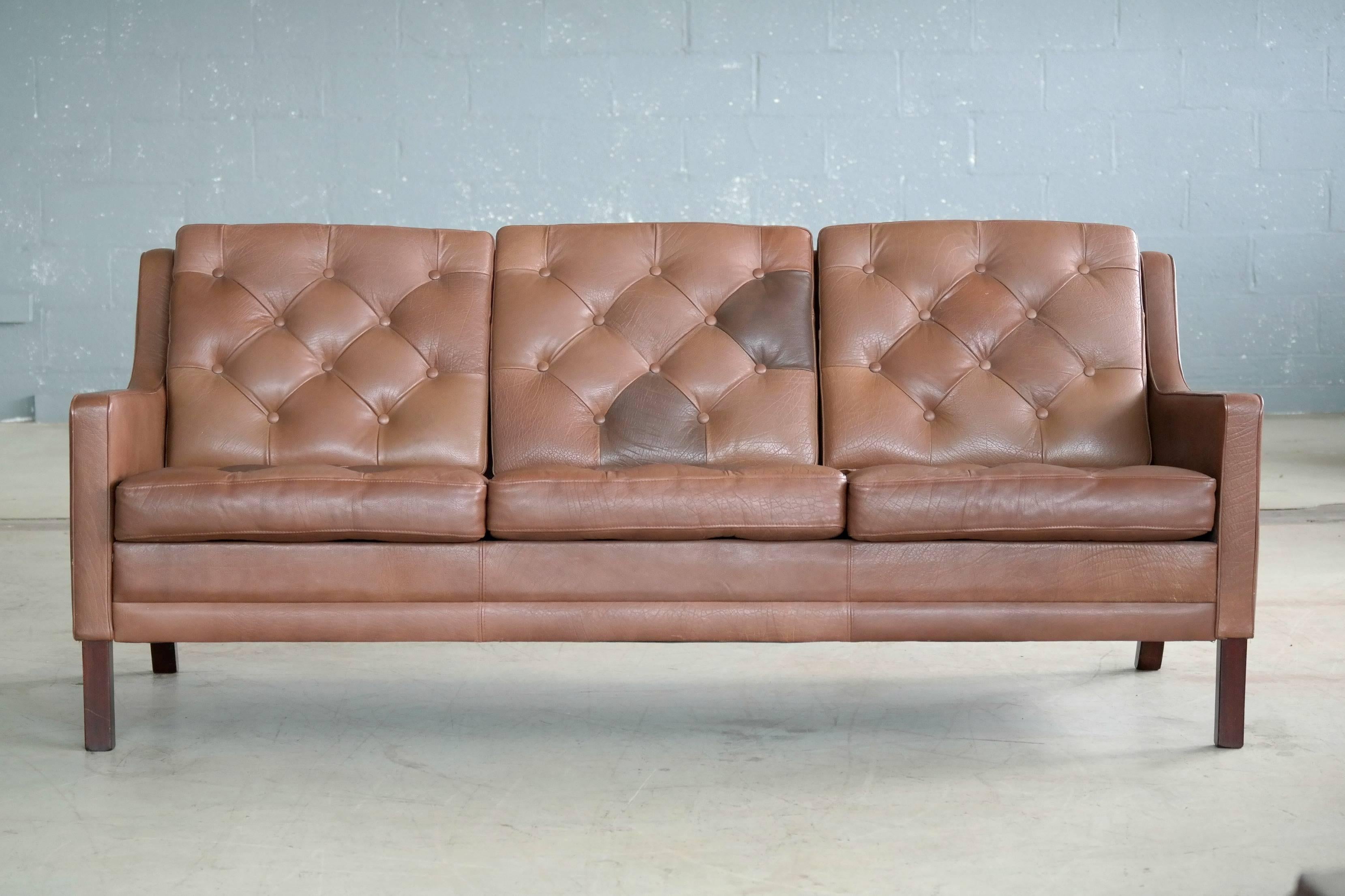 Great Ib Kofod-Larsen design with beautifully tufted patchwork cushions with leather buttons. Nice buffalo leather in very good condition. The sofa has nice patina and no cracking or crazing but the color it not quite uniform as some of the leather