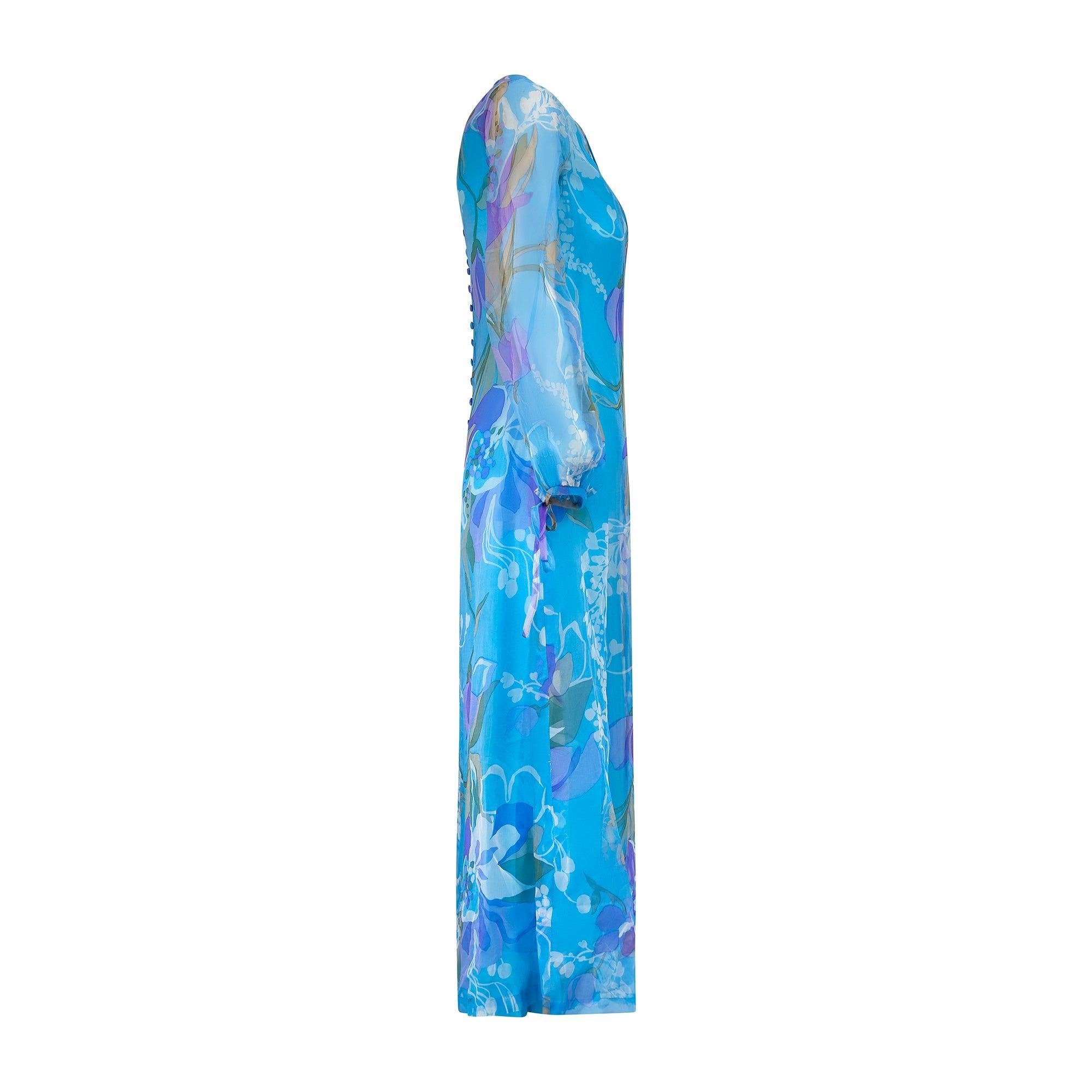 Cette robe longue couture des années 1960 est confectionnée en organza de soie avec un imprimé tourbillonnant de fleurs, de feuilles et de vignes dans des tons bleus, verts et violets. Il présente une coupe en A et tombe à la longueur des chevilles.