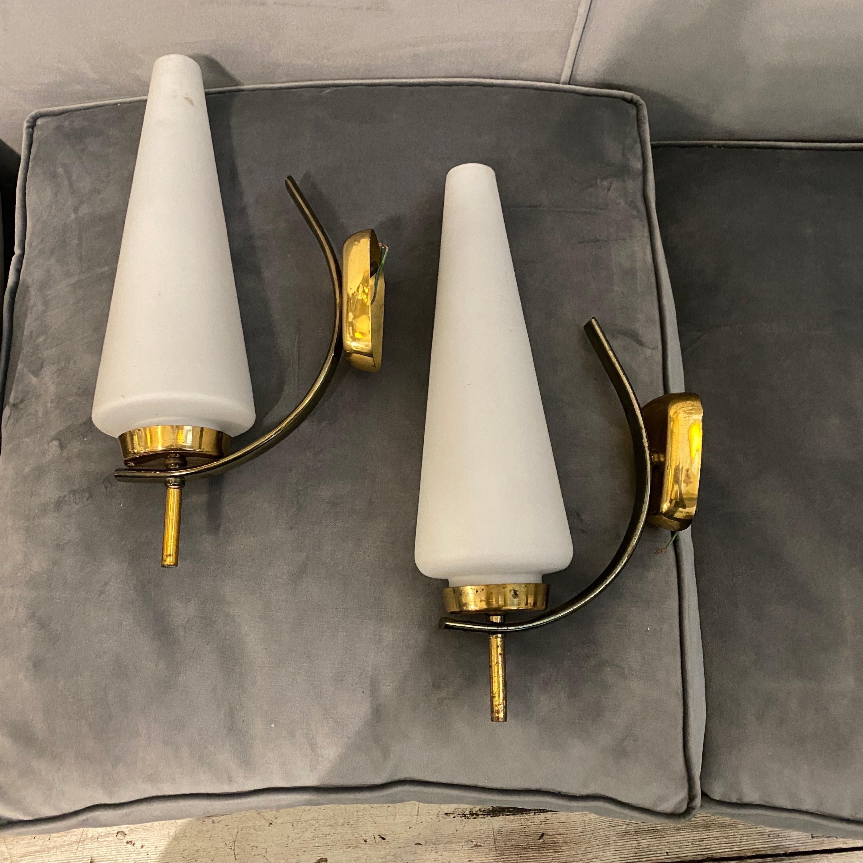 Two Italian wall sconces designed and manufactured in the Sixties in Italy in the manner of Stilnovo, they have been checked by an electrician, work both 110-240 volts and need regular e 14 bulbs. Brass it's in original patina, white glass diffusors