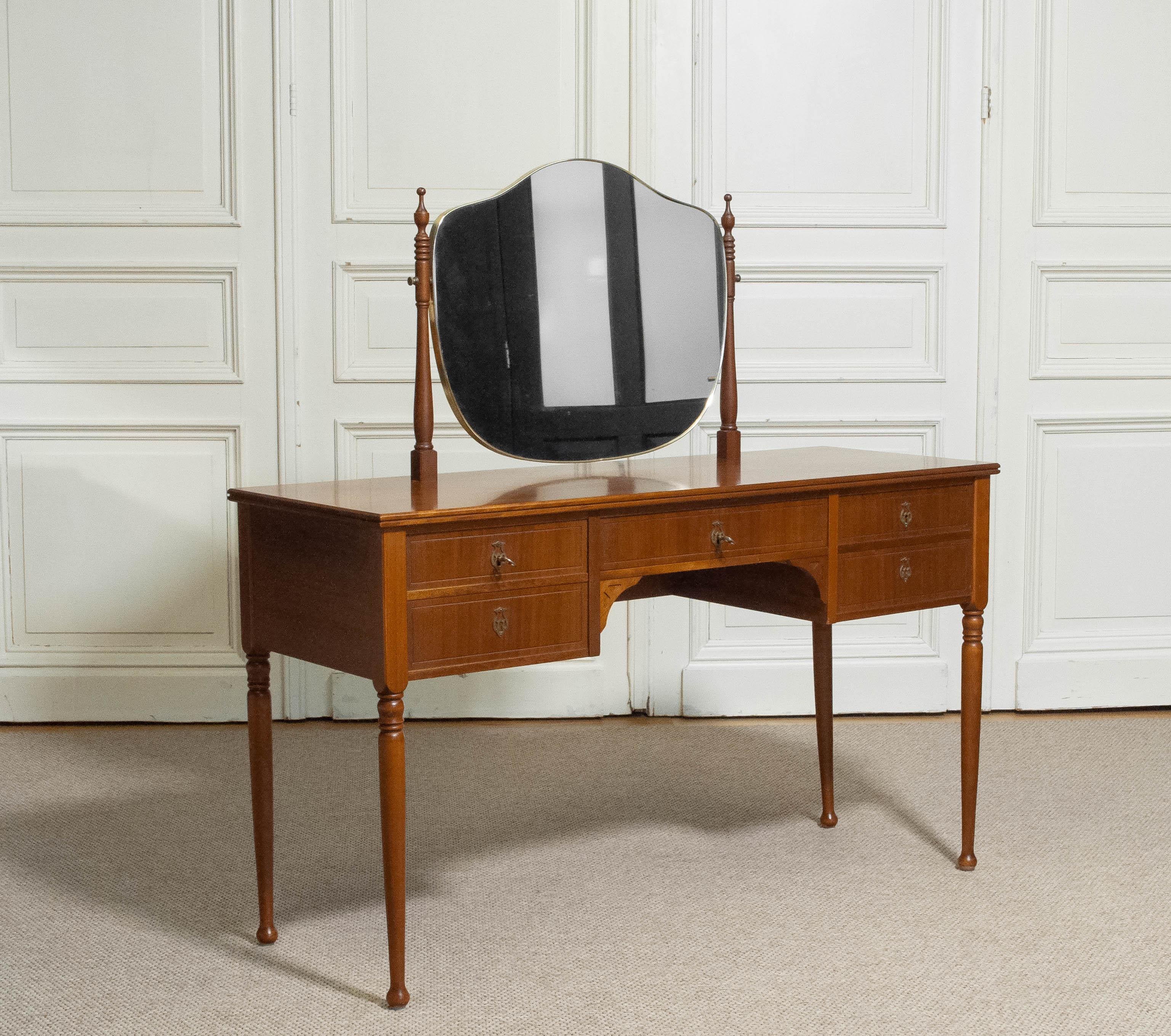 A refined 1960s mahogany vanity table in the elegant Biedermeier style. The piece is finely crafted with clean, harmonious lines and veneered on all sides, allowing it to stand freely in any interior. It is fitted with a practical arrangement of