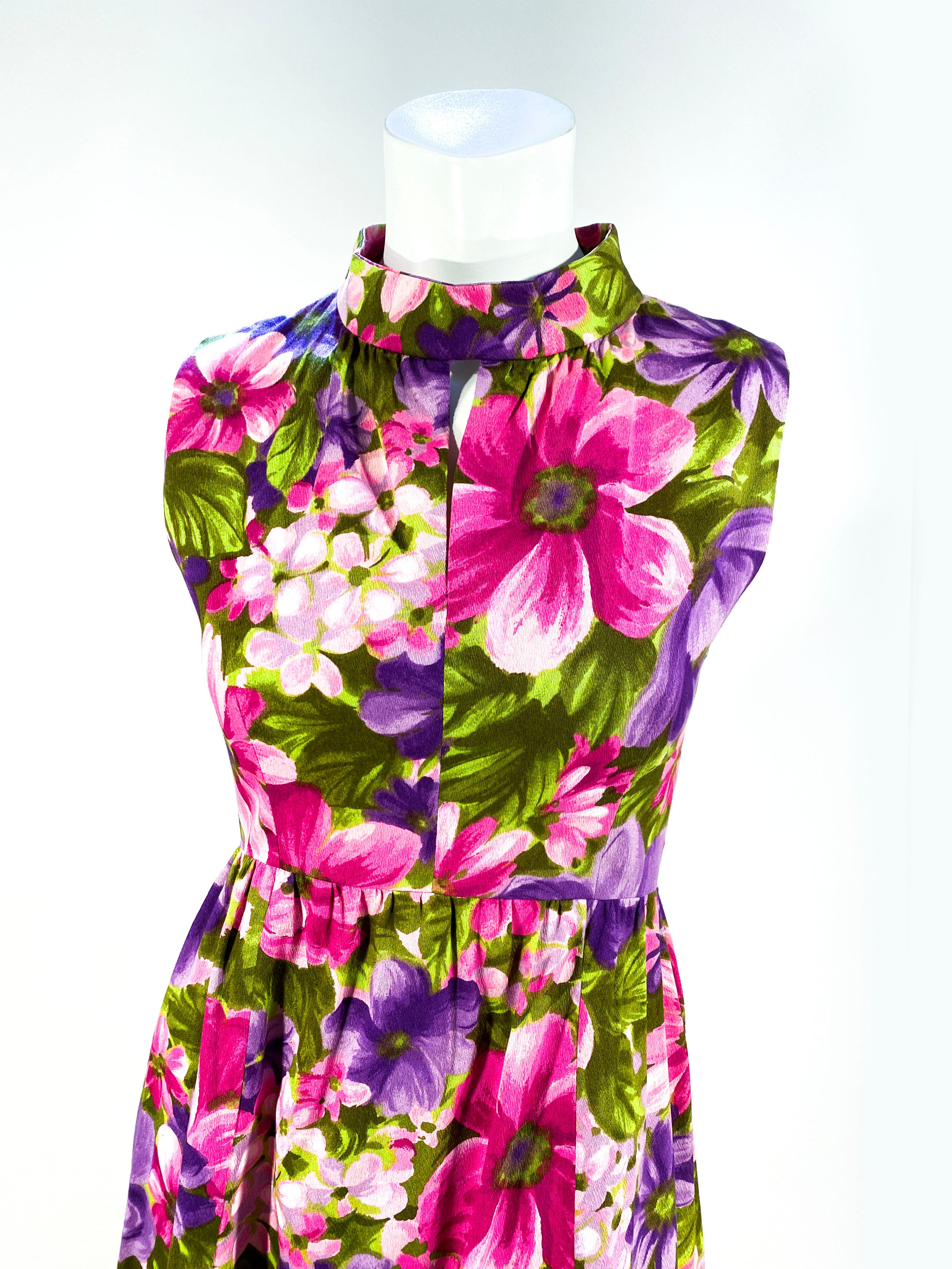 1960s dress featuring an impressionist floral print in vibrant sades of purple, pink, and green. The bodice has a mock turtle neck and a keyhole opening cut out. The fabric is a medium weight cotton.