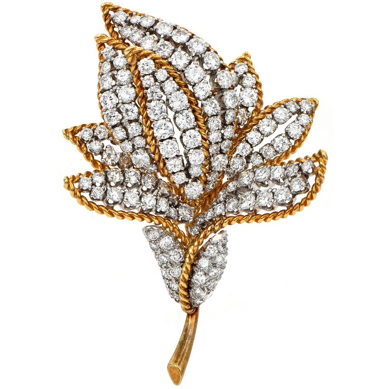 This breathtaking vintage brooch pin is from circa the late 1960s. This diamond flower brooch pin is hand-crafted in solid 18K yellow gold and solid platinum. Featuring a gorgeous blooming flower with leaves coming from the stem, this elegant pin is