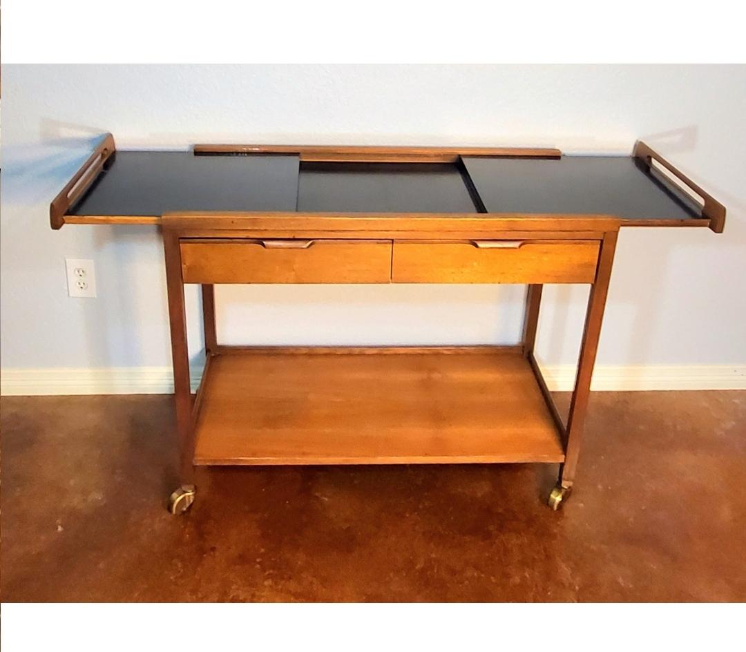 Classic Mid-Century Modern walnut expandable rolling bar cart or server, Manufactured by American of Martinsville, designed by Merton L. Gershun. Expanding black laminate sliding top opens to 56 inches, two drawers. Solid walnut construction,