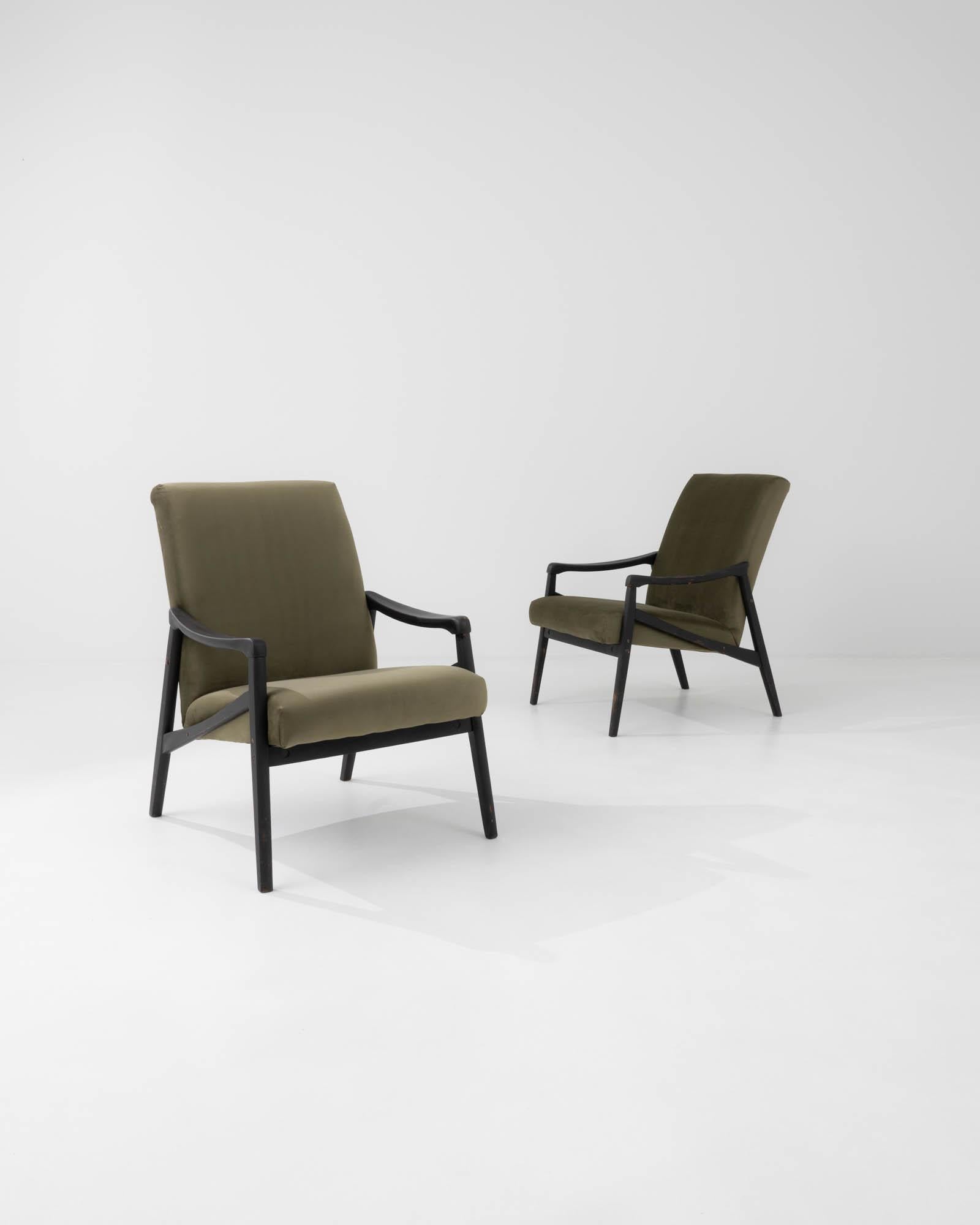 Paire de fauteuils produits dans l'ancienne Tchécoslovaquie, dont le design est attribué à Jiri Jiroutek. Le design des années 1960 est recouvert d'un velours vert olive lisse, associé à un bois dur délicatement patiné pour une fluidité sans effort.