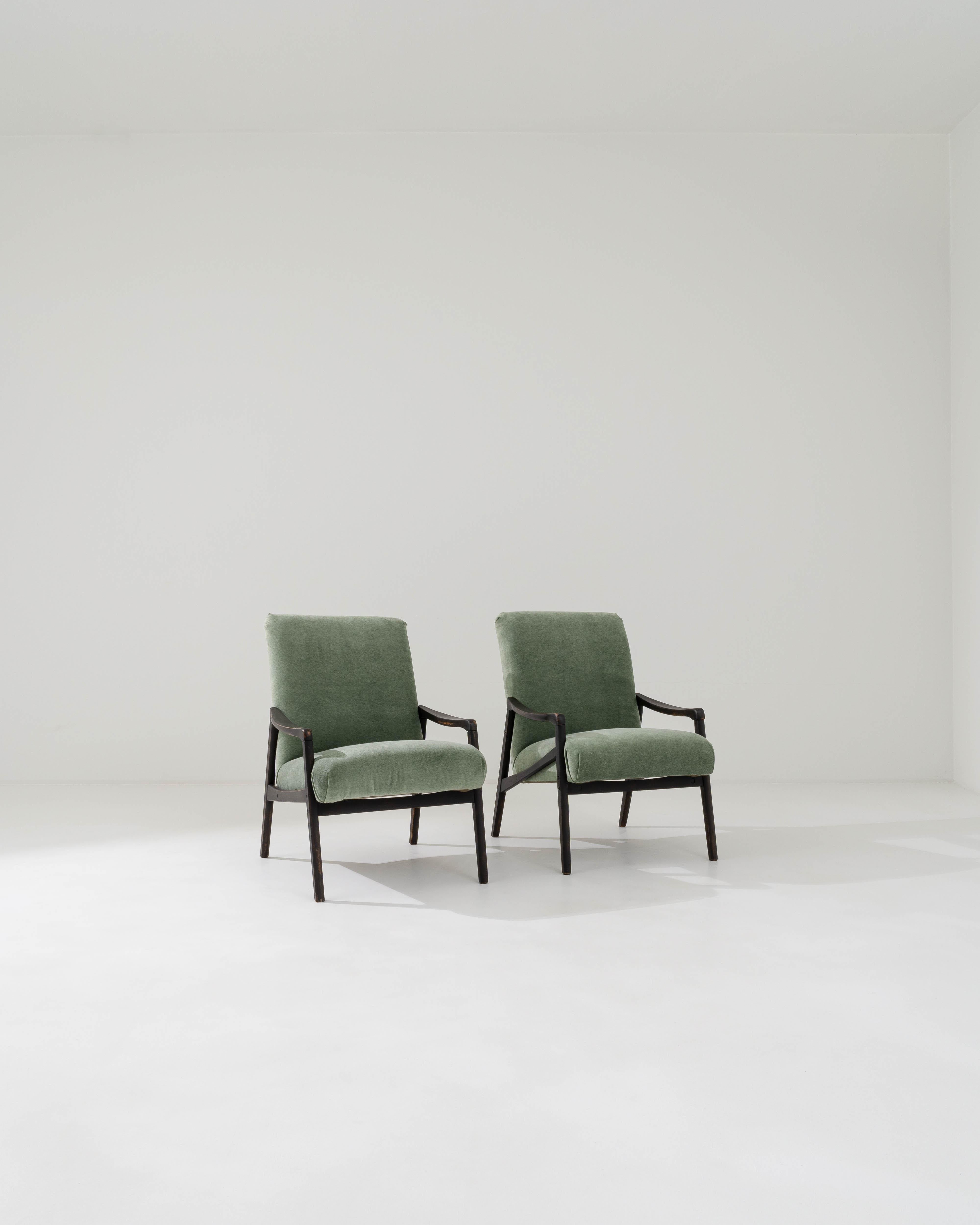 A pair of armchairs produced in the former Czechoslovakia, with the design attributed to Jiri Jiroutek. This 1960s design has been given a fresh look with velvety green reupholstery; the mossy hue softening the polished patina of the black hardwood